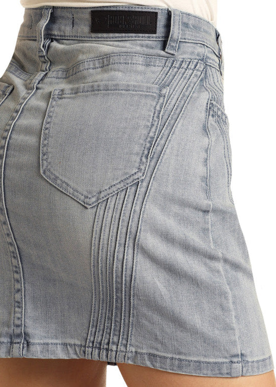 Close-up of a person wearing the Rock & Roll Denim High Waisted Pintuck Denim Mini Skirt with decorative stitching and a back pocket, photographed from the side and back against a plain background.