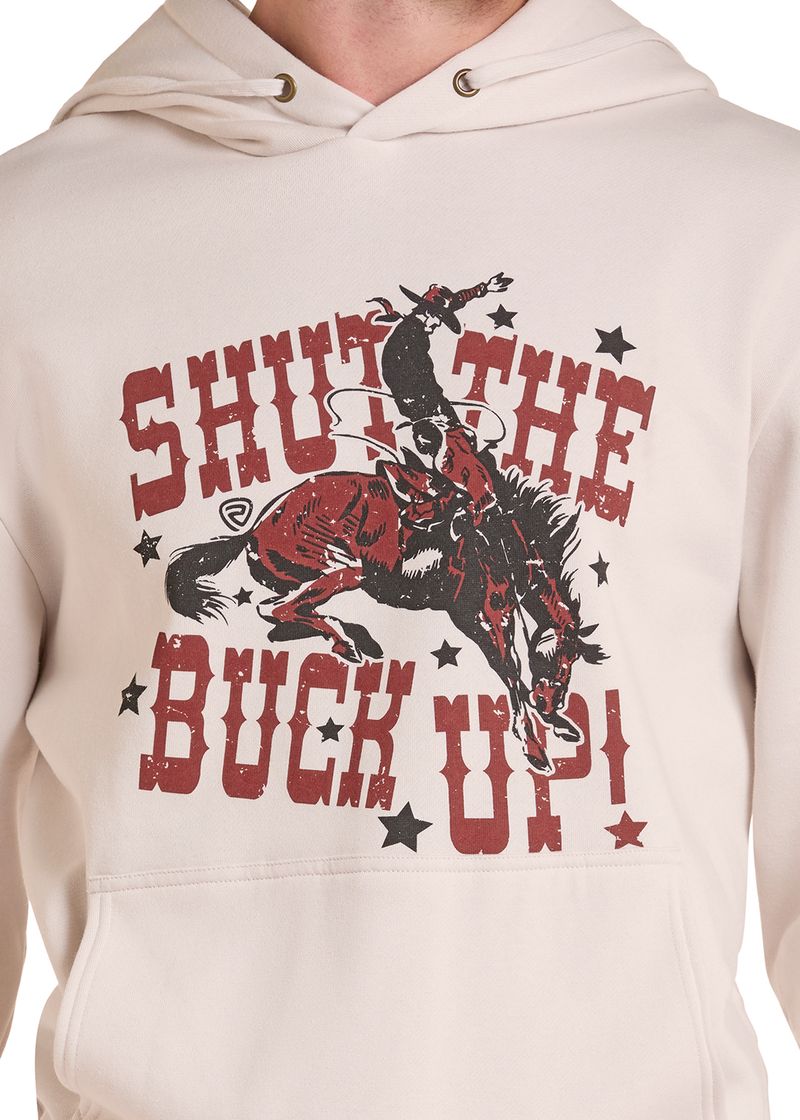 A close-up of a cream-colored hoodie featuring a graphic print of a cowboy riding a bucking horse with the text 'SHUT THE BUCK UP!' in distressed red lettering and black stars.