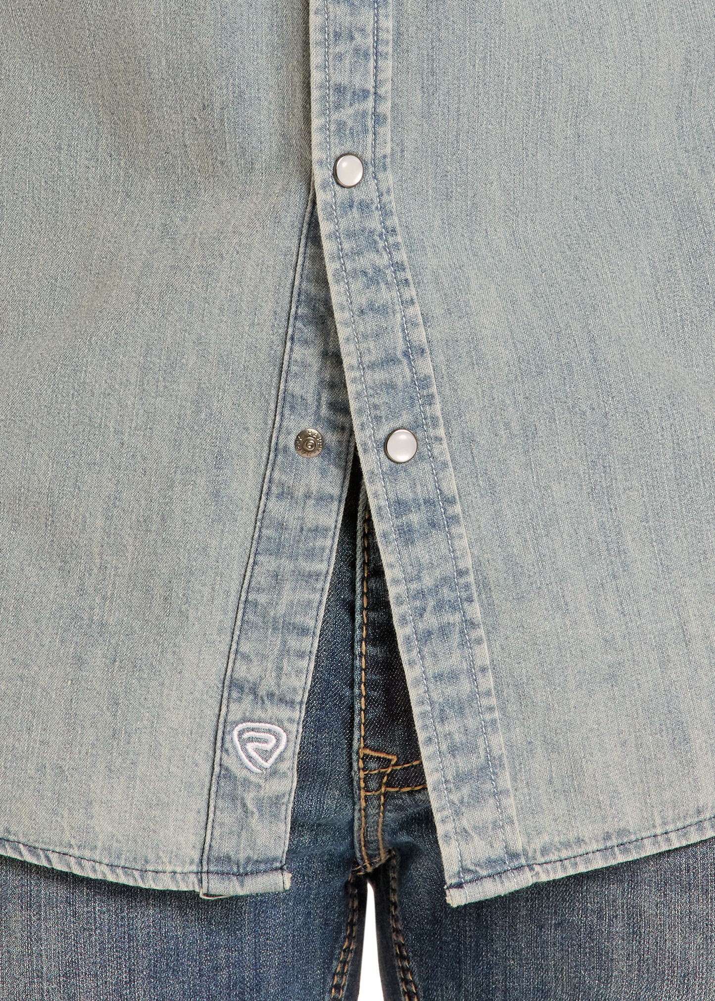 Close-up of the lower part of the Rock & Roll Denim Slim Fit Medium Wash Denim Snap Shirt with silver snap buttons, worn over blue jeans. A small embroidered logo is visible near the hem.