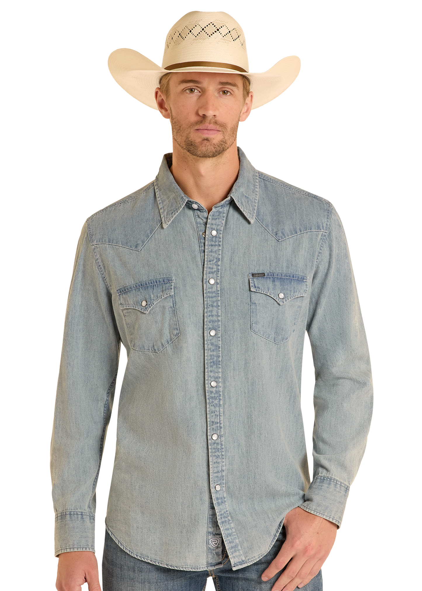A man wearing a Rock & Roll Denim Slim Fit Medium Wash Denim Snap Shirt stands facing forward with one hand in his pocket, paired with blue jeans and a cream cowboy hat, against a plain background.
