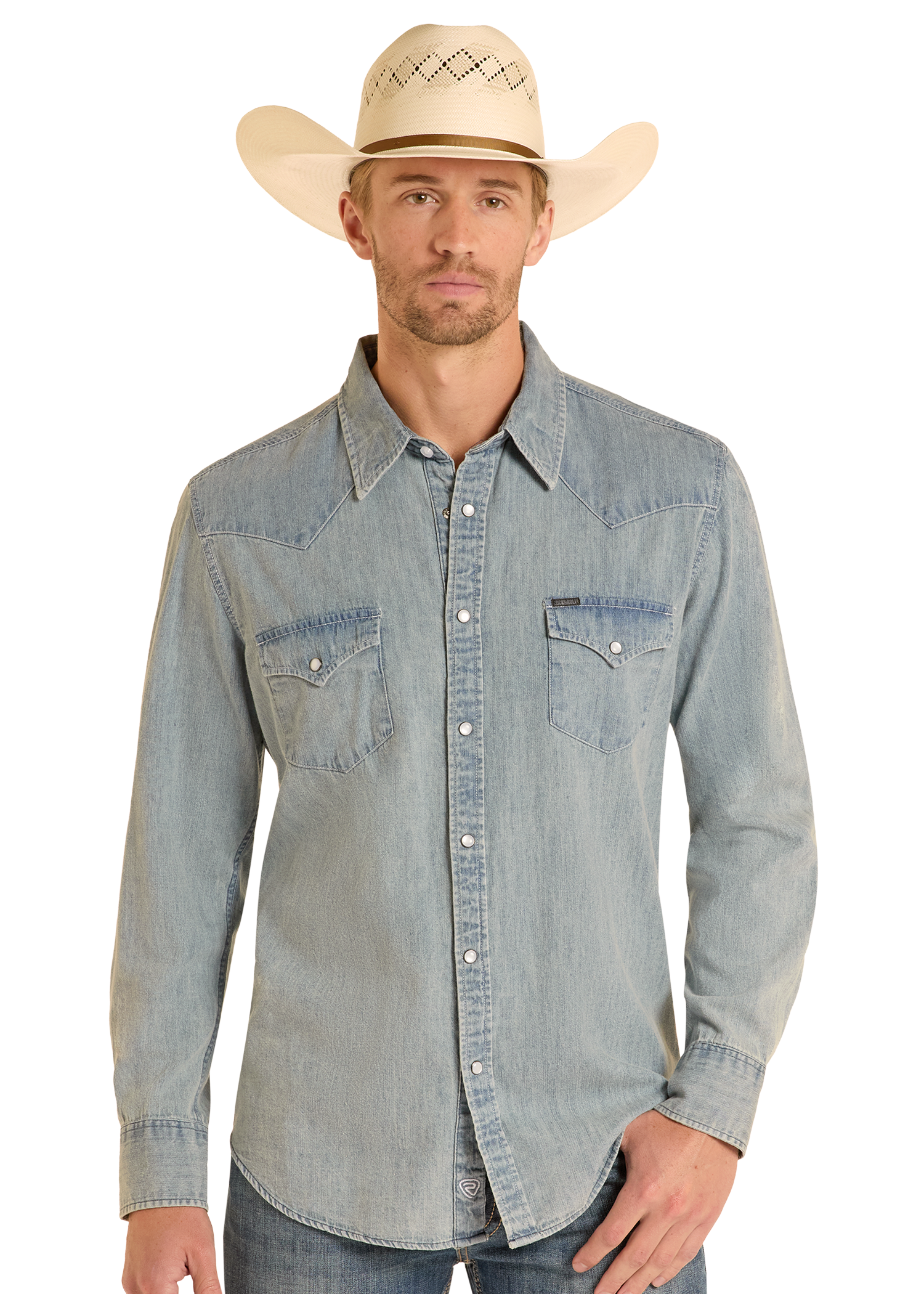 A man wearing a Rock & Roll Denim Slim Fit Medium Wash Denim Snap Shirt stands facing forward with one hand in his pocket, paired with blue jeans and a cream cowboy hat, against a plain background.