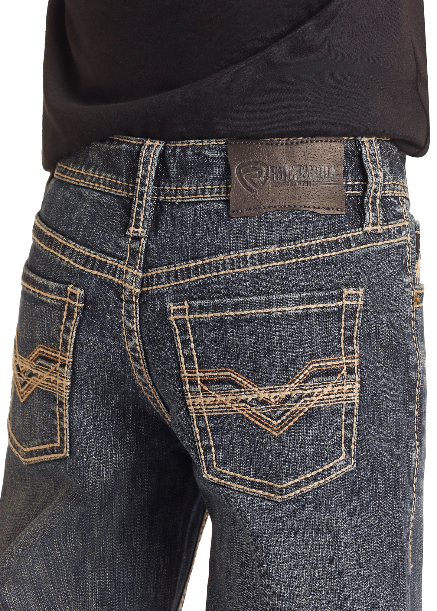 Close-up of a person wearing Rock & Roll Denim Boys' Regular Fit Raised Embroidery Bootcut Jeans in dark blue, featuring tan stitching, decorative pocket designs, and a black leather patch on the waistband under a black shirt.