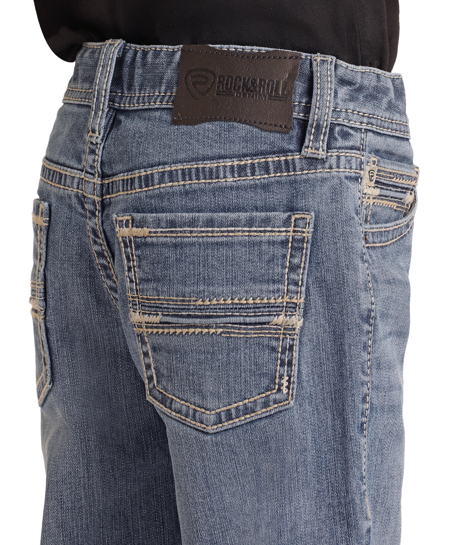 A close-up shows a person in a black shirt tucked into Boys' Regular Fit Two-Tone Embroidered Bootcut Jeans by Rock & Roll Denim, featuring detailed stitching and a black brand patch above the right pocket.
