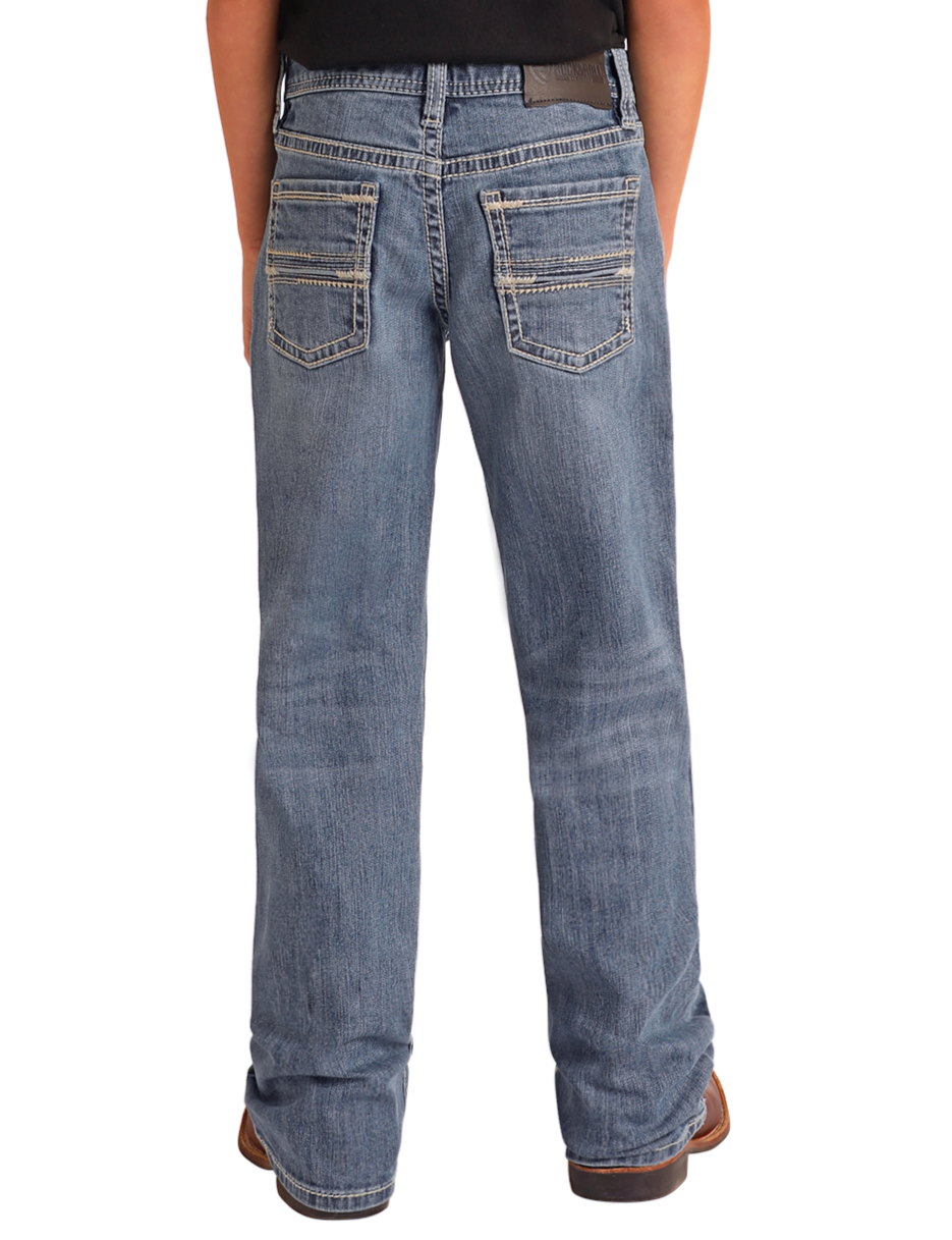 A person is shown from the back wearing Rock & Roll Denim Boys' Regular Fit Two-Tone Embroidered Bootcut Jeans with light stitching and decorative back pocket details, paired with brown shoes against a plain white background.