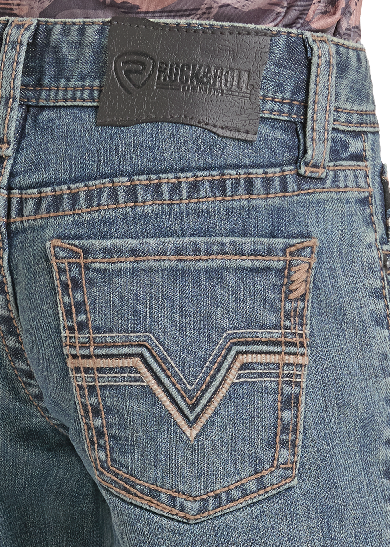 Close-up of the back waistband and pocket area of blue denim jeans, showing a black Rock & Roll branded leather patch and decorative contrast stitching on the back pocket.