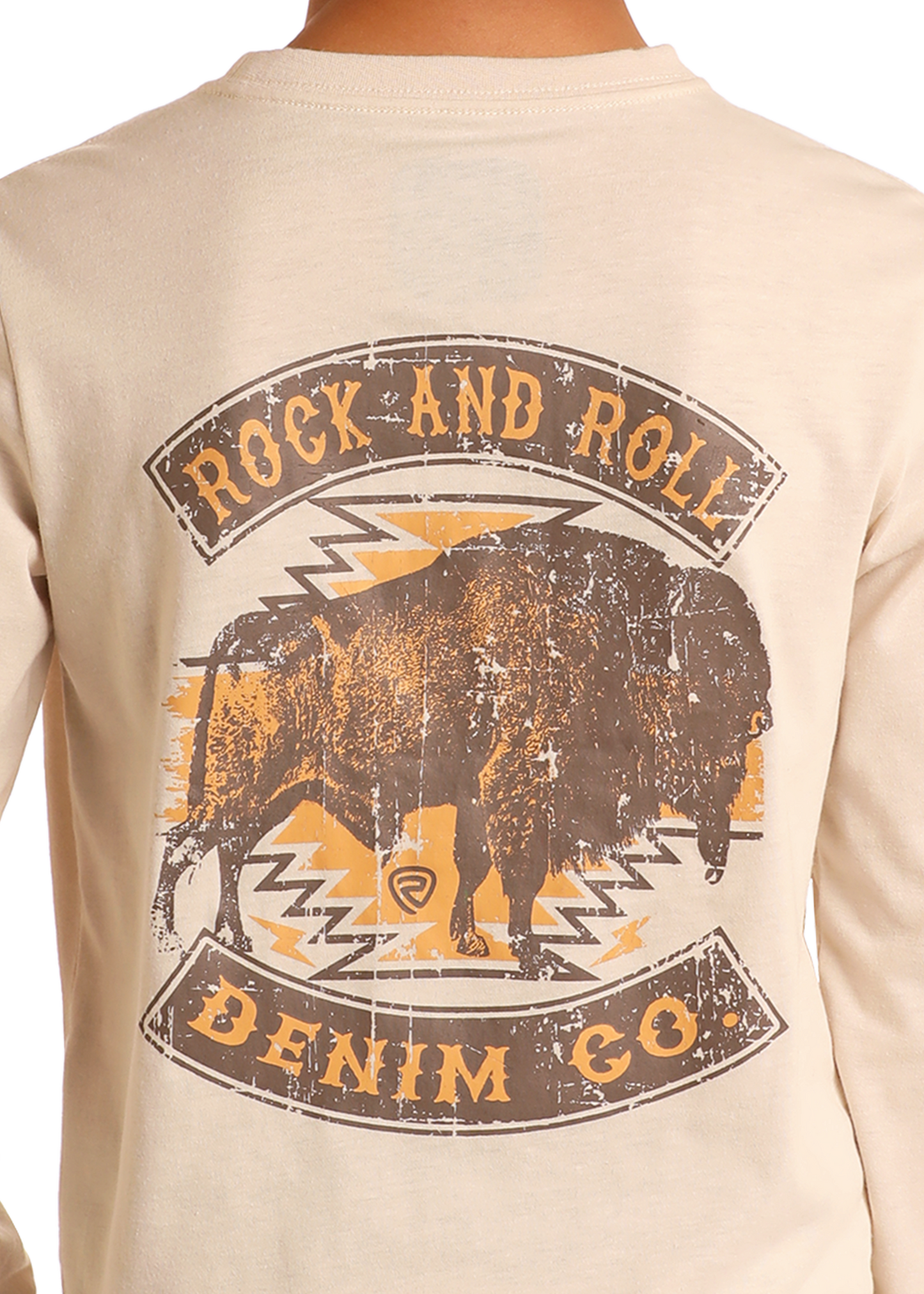A boy wears the Rock & Roll Denim Boys' Buffalo Graphic Long Sleeve Tee in beige, featuring a distressed buffalo graphic with geometric patterns and vintage-style branding on the back.
