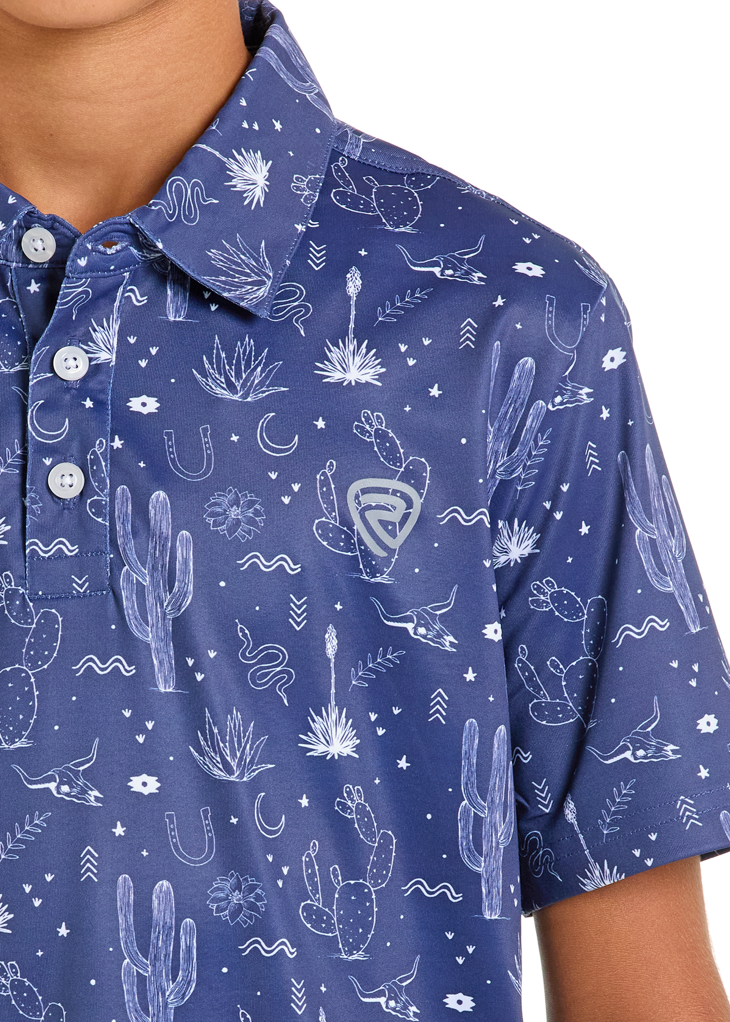 A close-up of the Rock & Roll Denim Boys' Blue Conversation Print Polo, featuring white buttons and a pattern of cacti, steer skulls, horseshoes, snakes, stars, and southwestern plants worn by a boy.