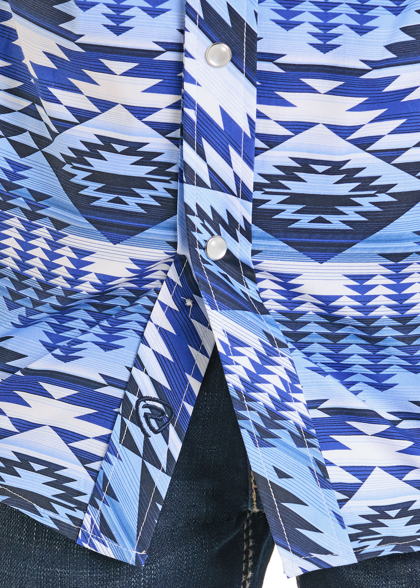 A Rock & Roll Denim Boys' Blue Aztec Print Long Sleeve Snap Shirt with blue and white geometric patterns and pearl snap buttons, worn partially unbuttoned over dark denim jeans.