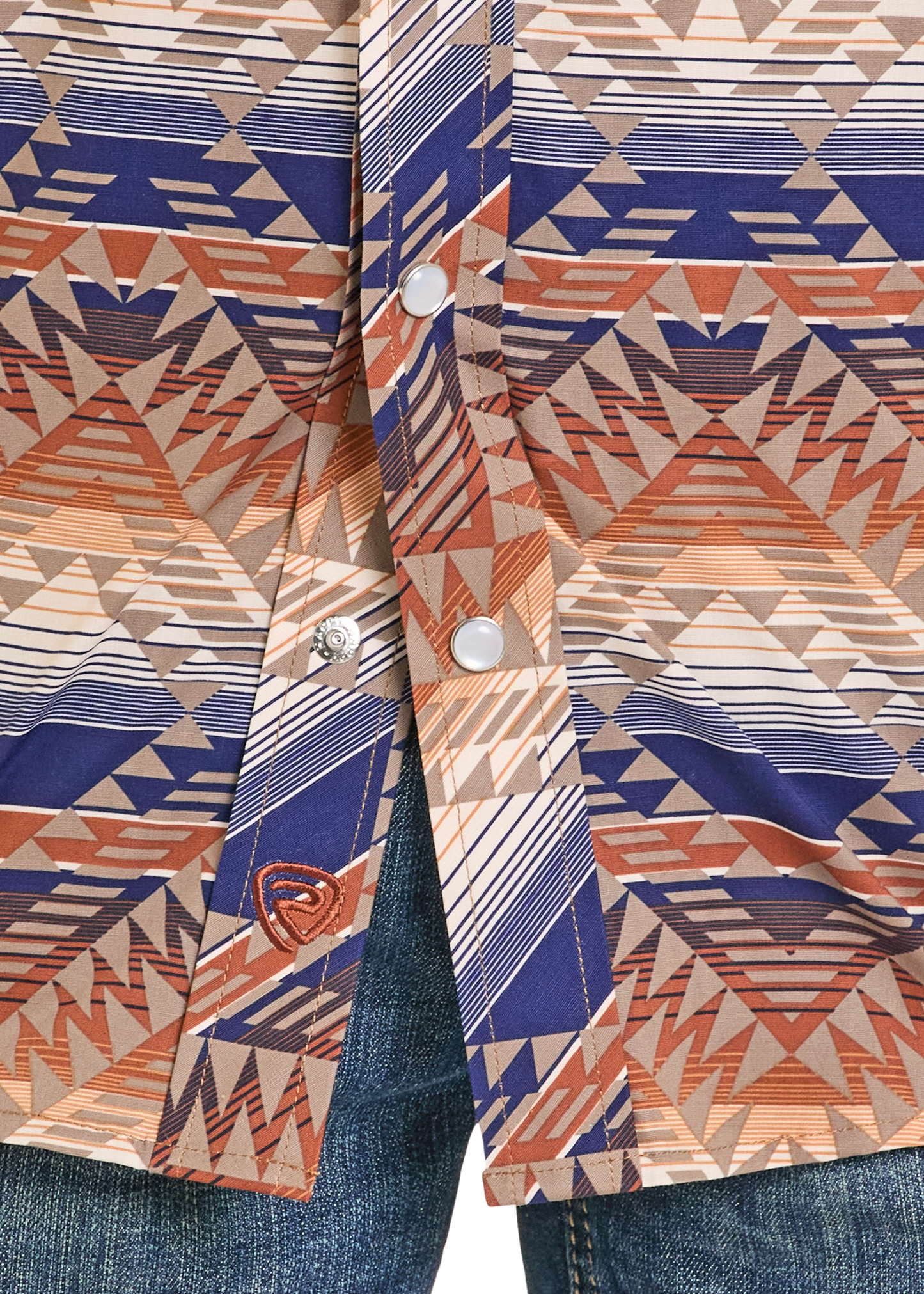 Close-up of the Rock & Roll Denim Boys' Multi Aztec Long Sleeve Snap Shirt featuring a southwestern-style geometric pattern in brown, tan, orange, and navy blue, paired with blue denim jeans.