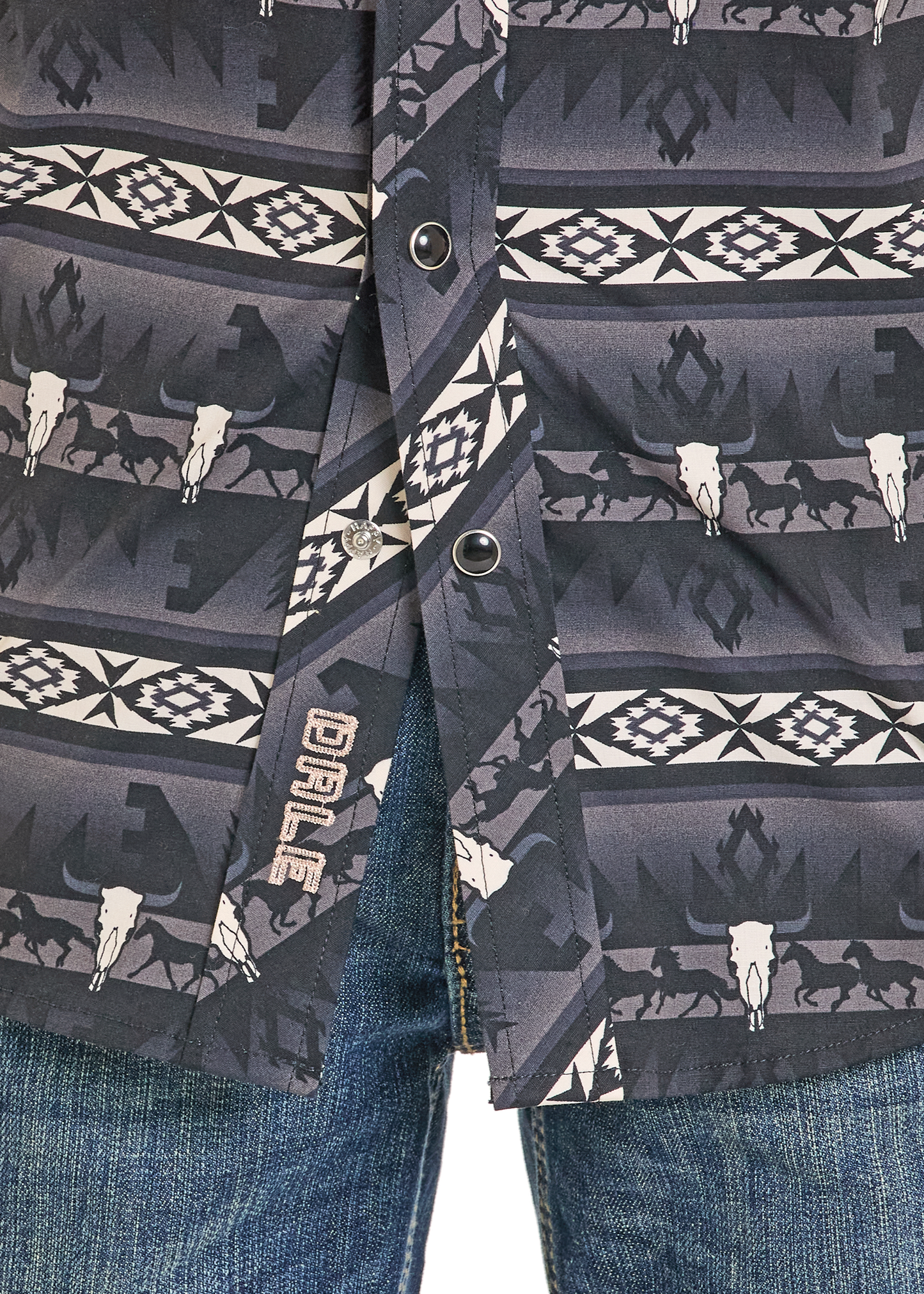 Close-up of the Rock & Roll Denim Boys' Dale Brisby Black Aztec Long Sleeve Snap Shirt, featuring a southwestern pattern with cattle skulls and horse silhouettes, paired with blue jeans.
