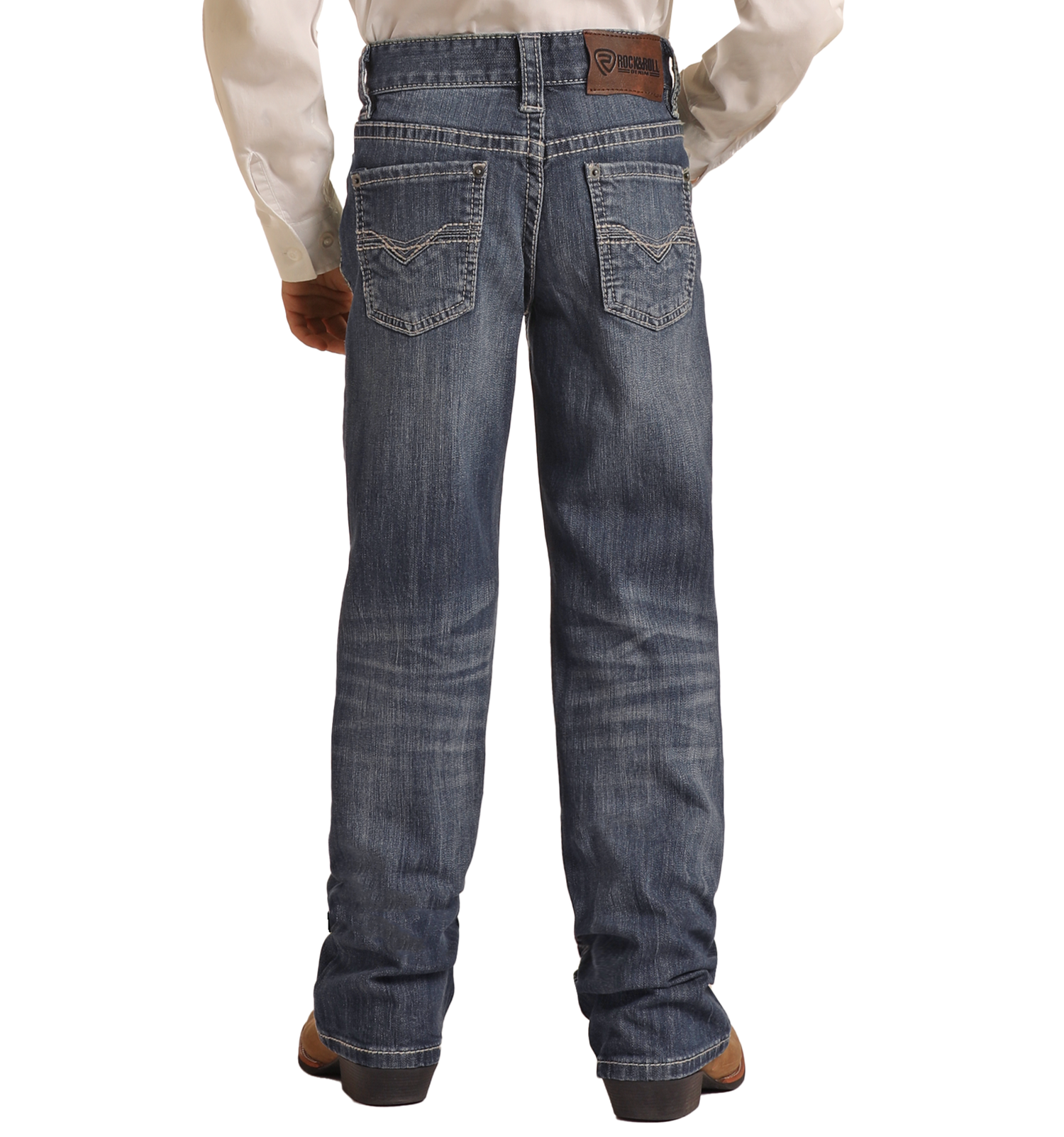 A man models Rock & Roll Denim Boys' Regular Fit Bootcut Jeans with light grey top-stitching on the back pockets, paired with brown boots and a white shirt, shown from behind.