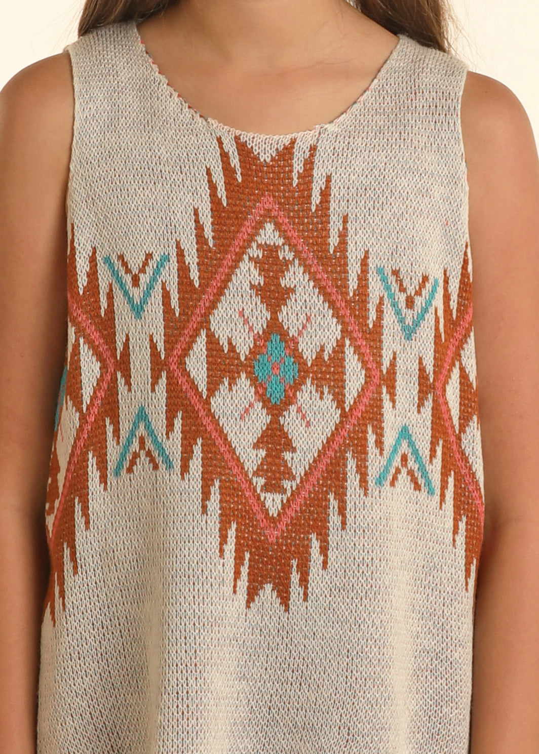 A young person wears the Girls' Aztec Knit Tank by Rock & Roll Denim—a beige, sleeveless top with bold orange, turquoise, and white geometric patterns. The photo is cropped from shoulders to waist to highlight this Southwestern-inspired style.