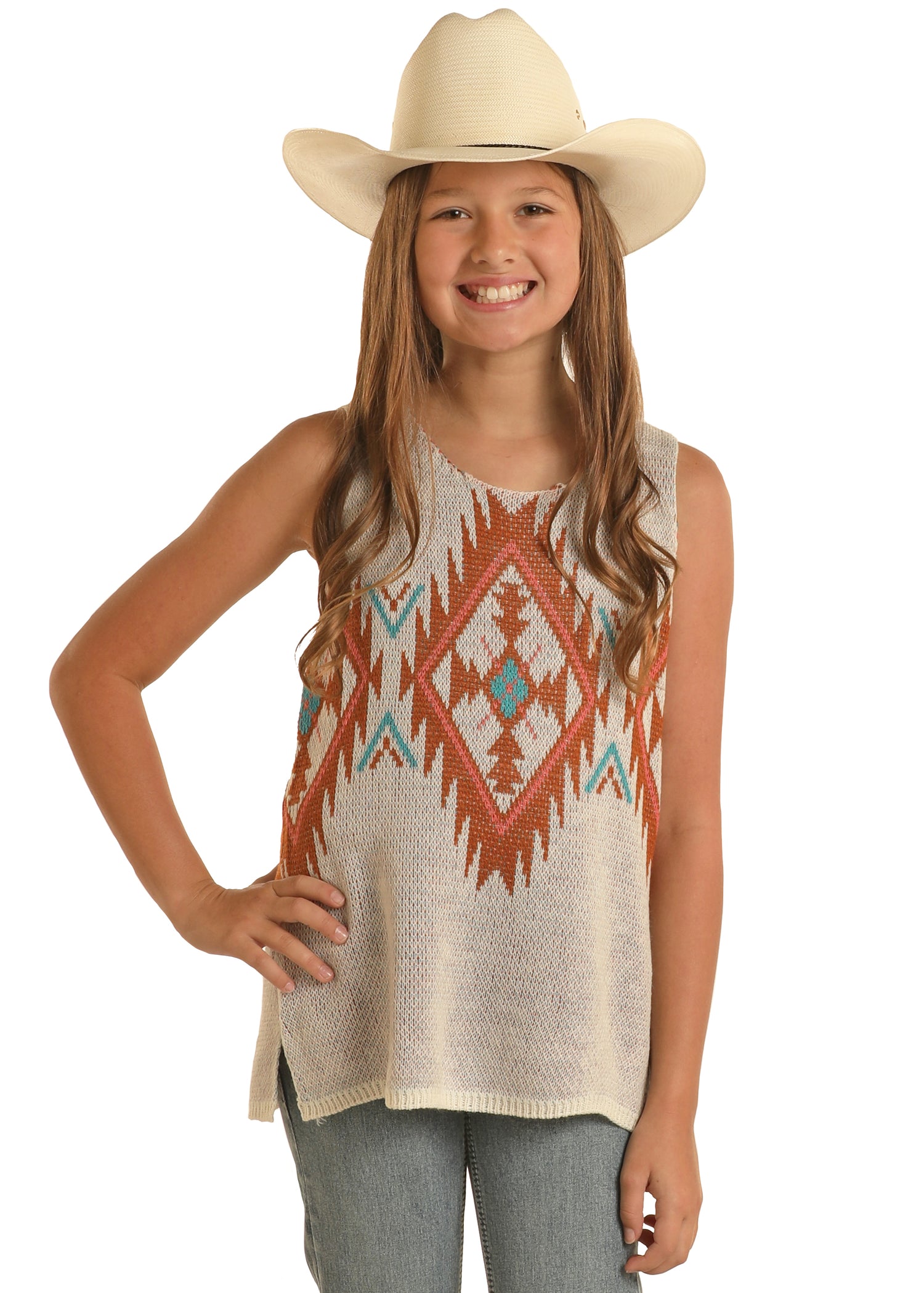 A smiling girl stands with one hand on her hip against a white background, wearing a white cowboy hat, blue jeans, and the Rock & Roll Denim Girls' Aztec Knit Tank featuring a colorful geometric pattern.