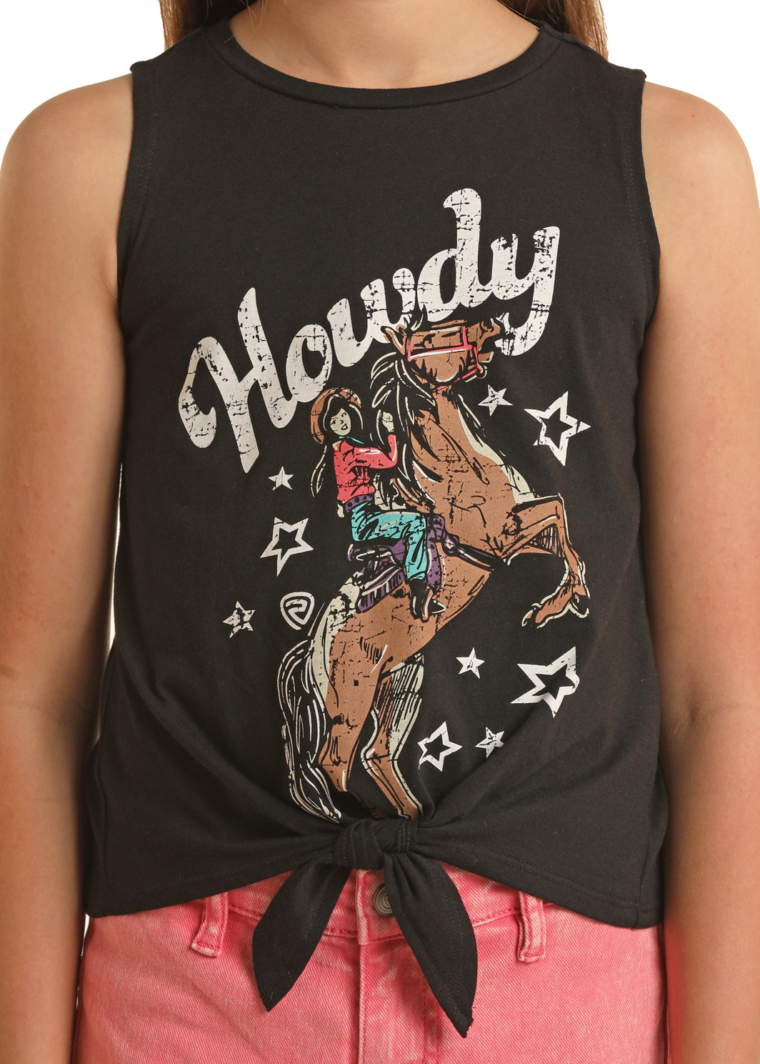 A girl wears Rock & Roll Denim's Girls' Howdy Graphic Tank with a waist tie and pink shorts. The tank features “Howdy” above a cowboy riding a bucking horse, surrounded by stars.