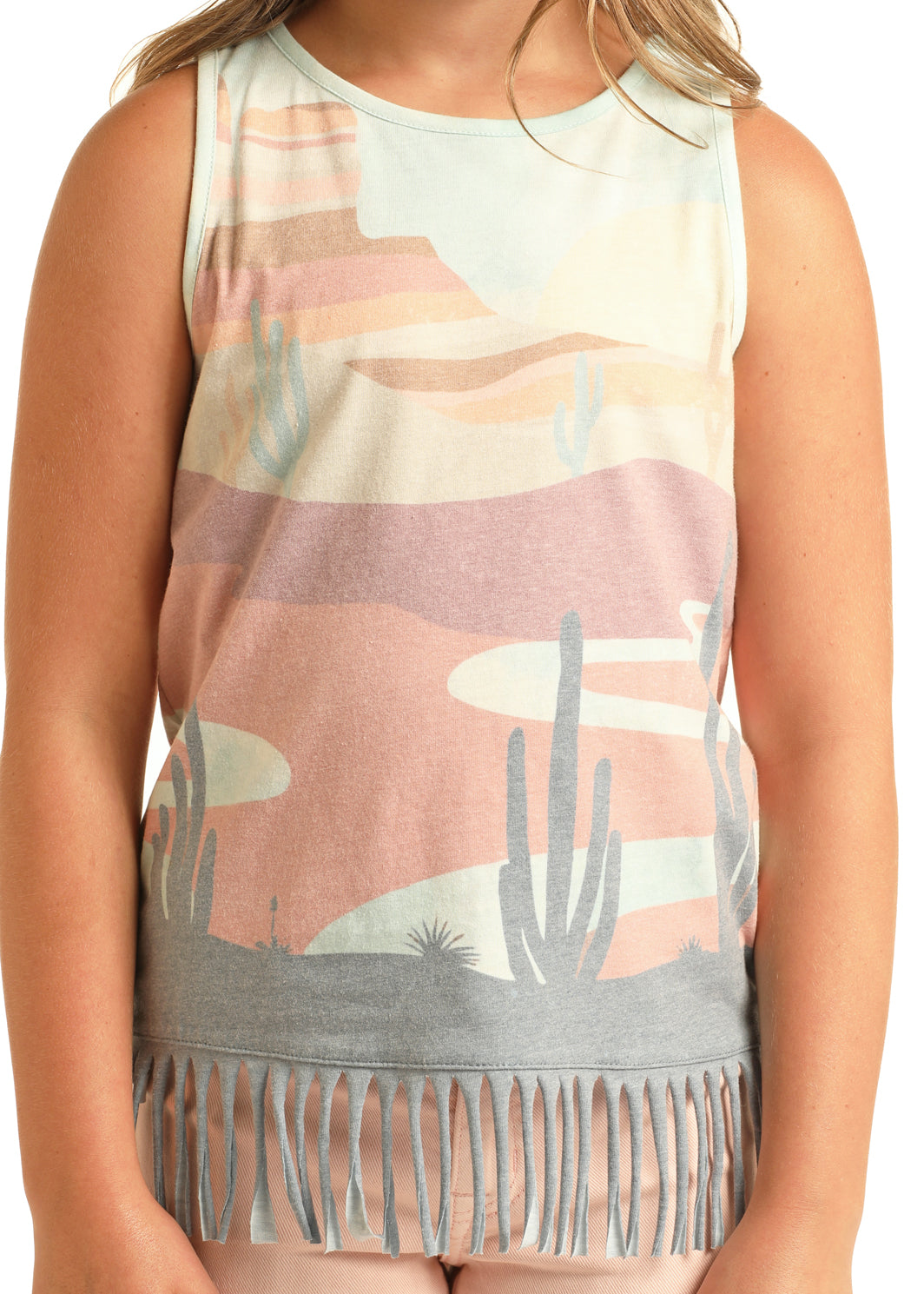 A child wears the Rock & Roll Denim Girls' Desert Scenery Fringe Tank, featuring a pastel desert landscape with cacti, abstract shapes in pink, gray, and beige, plus playful fringe at the hem for a fun western touch.