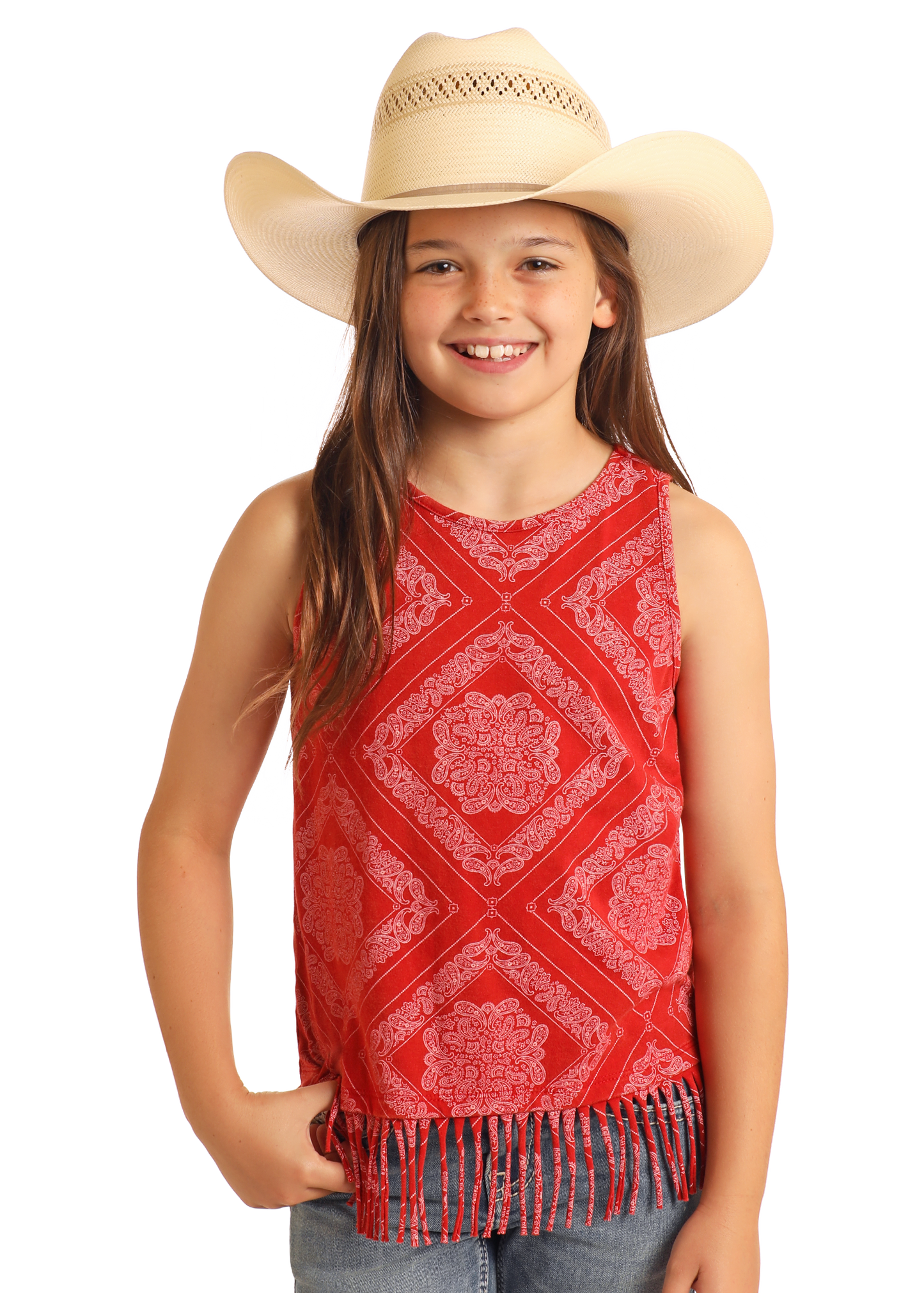 A smiling young girl wears the Rock & Roll Denim Girls' Bandana Fringe Tank—a sleeveless red bandana print top with a fringe hem—paired with blue jeans and a beige cowboy hat, standing against a white background.