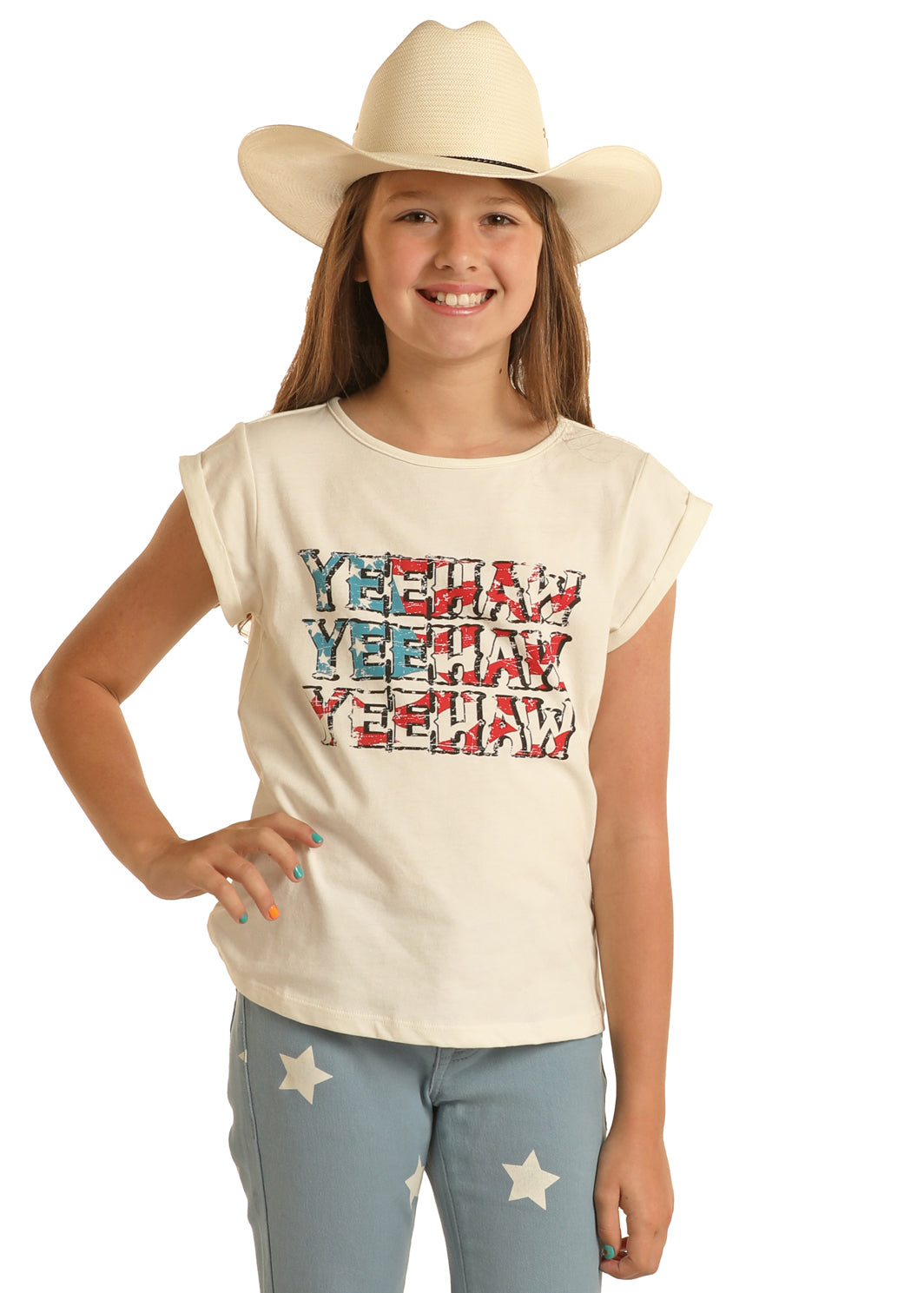 A smiling girl in a white cowboy hat and the Rock & Roll Denim Girls' American Flag Yeehaw Tee stands confidently with one hand on her hip, showing off her patriotic style against a white background.
