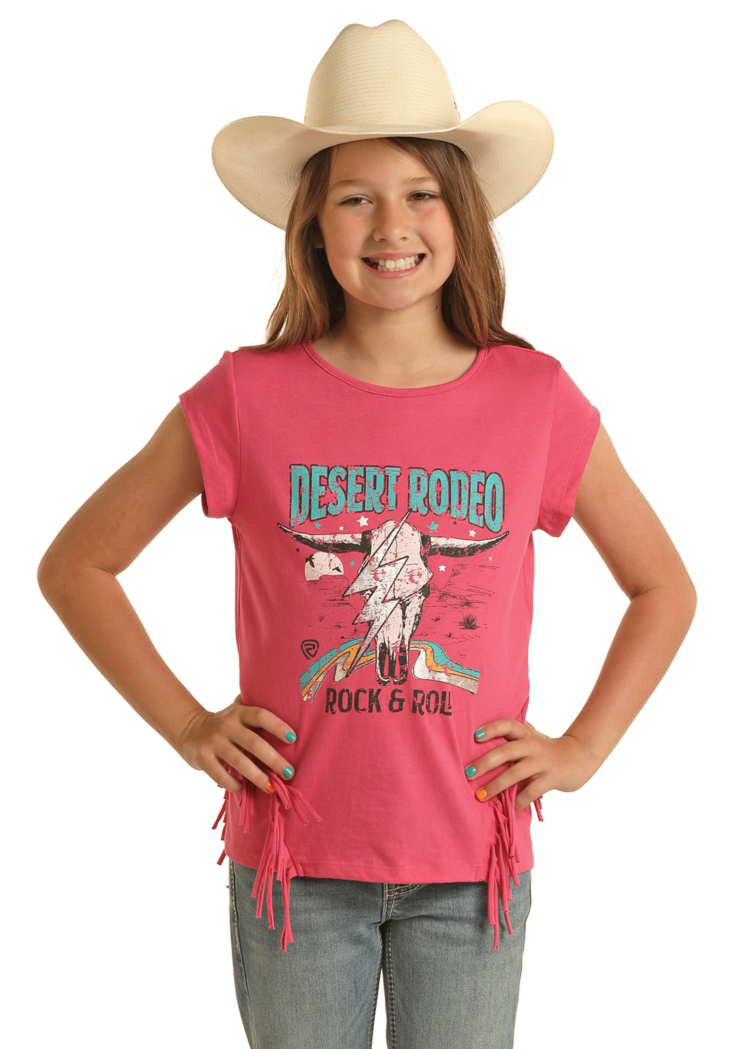 A smiling girl in a white cowboy hat and blue jeans models the Rock & Roll Denim Girls' Desert Rodeo Fringe T-Shirt, featuring a bold lightning skull graphic—a fun choice for rodeo-loving girls!.