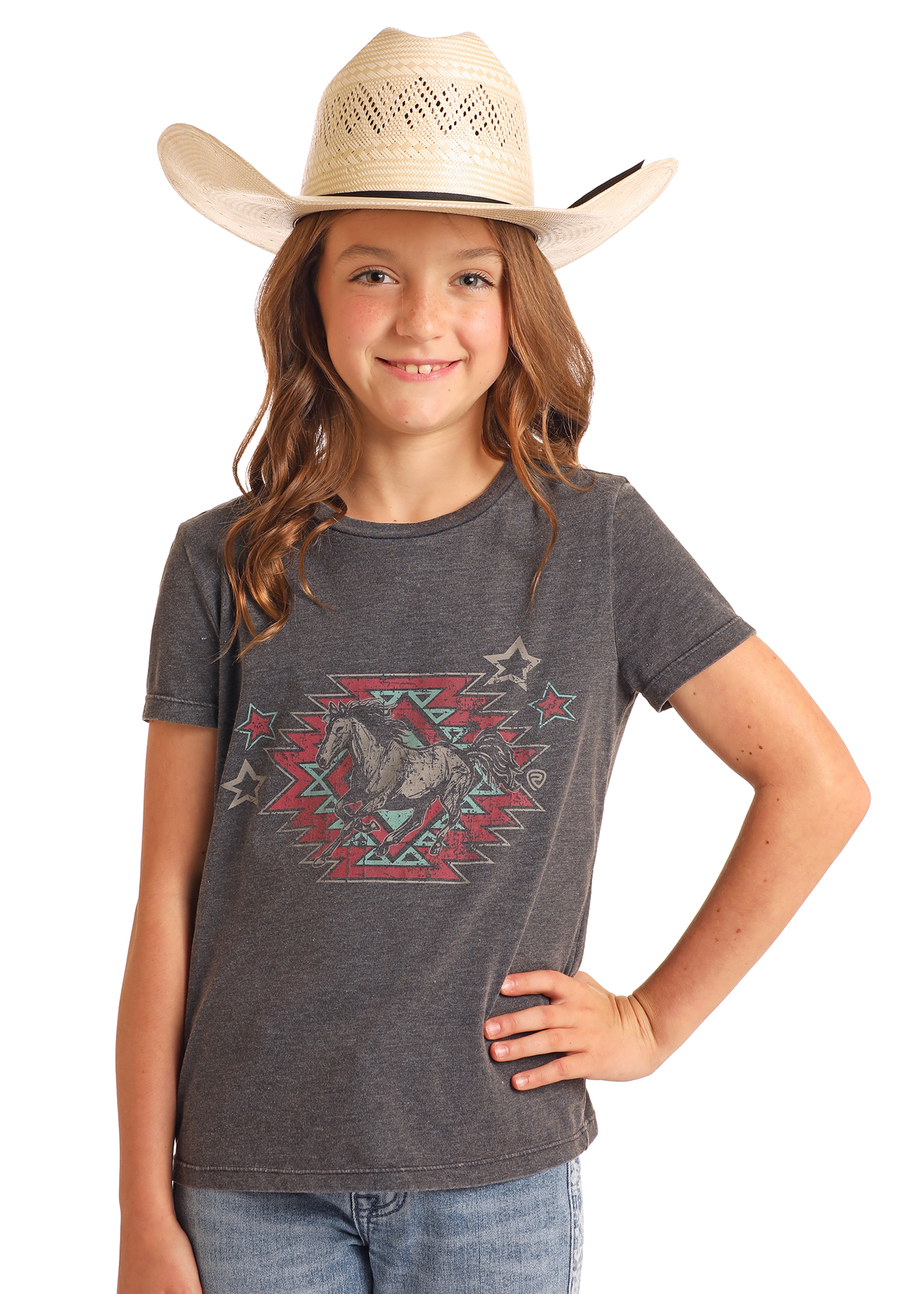 A girl wearing a straw cowboy hat, Rock & Roll Denim's Girls' Aztec Horse Graphic T-Shirt, and blue jeans stands with one hand on her hip, smiling at the camera against a plain background.