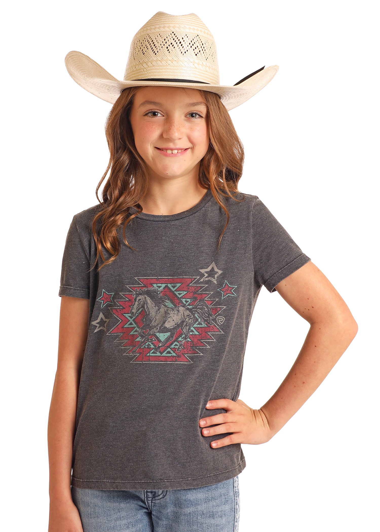 A girl wearing a straw cowboy hat, Rock & Roll Denim's Girls' Aztec Horse Graphic T-Shirt, and blue jeans stands with one hand on her hip, smiling at the camera against a plain background.
