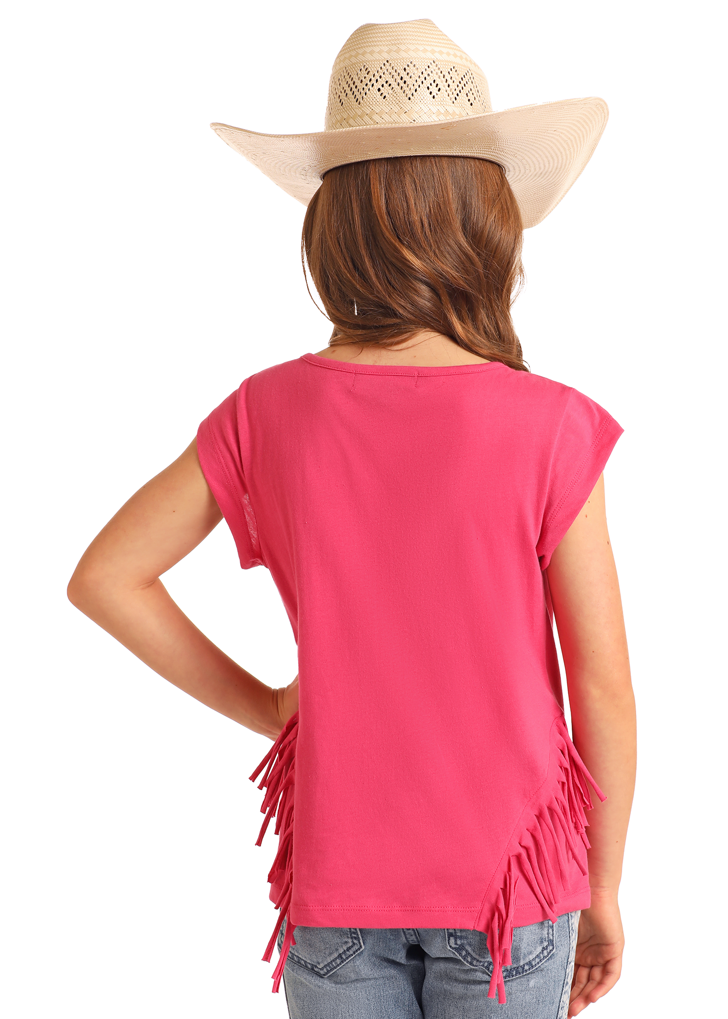 A young girl in a beige cowboy hat, blue jeans, and a Rock & Roll Denim Girls' Rhinestone Desert Graphic T-Shirt with bright pink fringe stands with her hand on her hip, facing away from the camera.