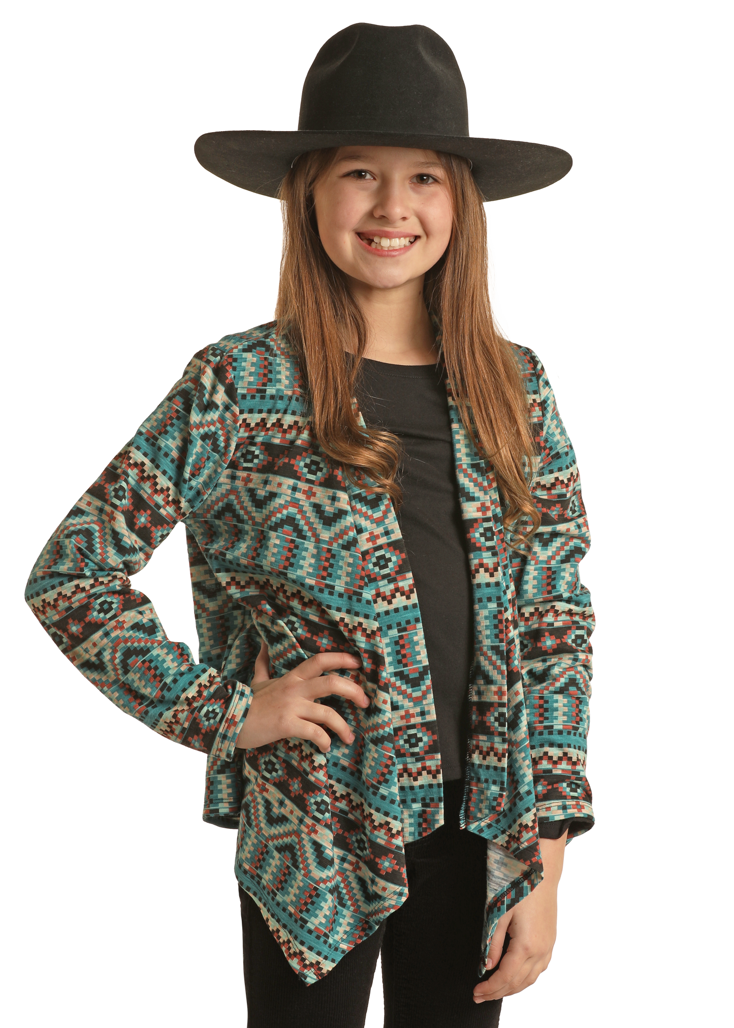 A smiling young girl wears a wide-brimmed black hat, black shirt, and Rock & Roll Denim Girls' Aztec Print Cardigan in blue, brown, and white, standing confidently with one hand on her hip against a white background.