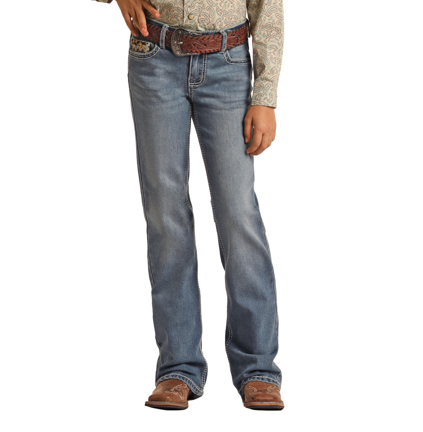 A person stands against a white background, shown from shoulders down, wearing Rock & Roll Denim Girls' Leopard Embroidered Pocket Bootcut Jeans, a patterned long-sleeve shirt, a brown woven belt, and brown cowboy boots.