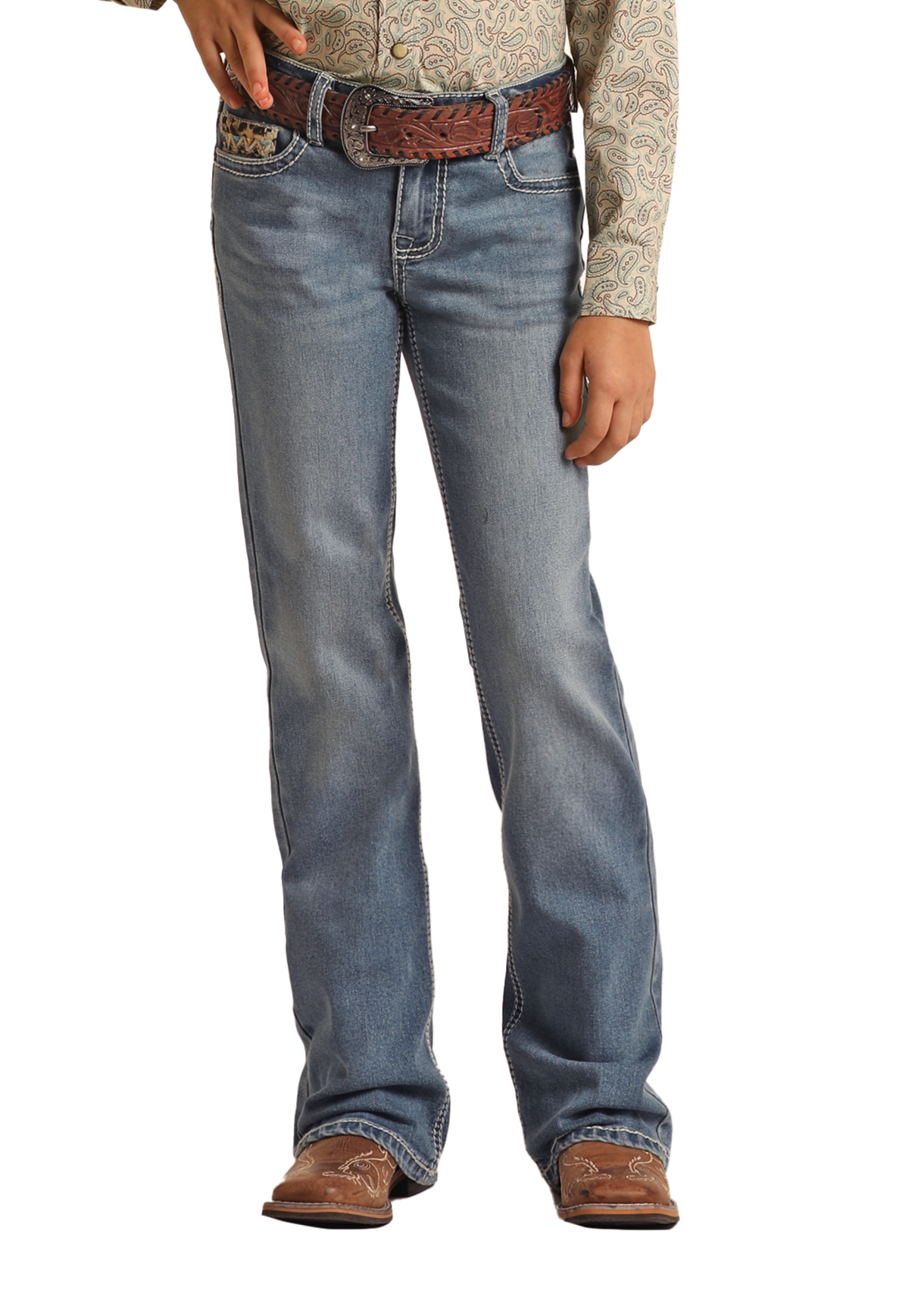 A person stands against a white background, shown from shoulders down, wearing Rock & Roll Denim Girls' Leopard Embroidered Pocket Bootcut Jeans, a patterned long-sleeve shirt, a brown woven belt, and brown cowboy boots.