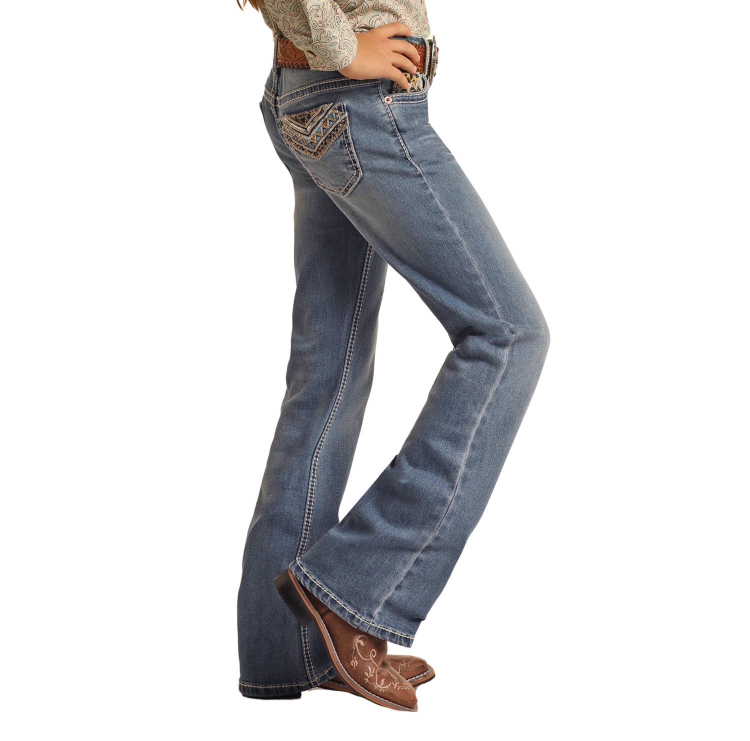 A girl wearing Rock & Roll Denim Girls' Leopard Embroidered Pocket Bootcut Jeans and brown cowboy boots stands sideways with her hands on her hips.