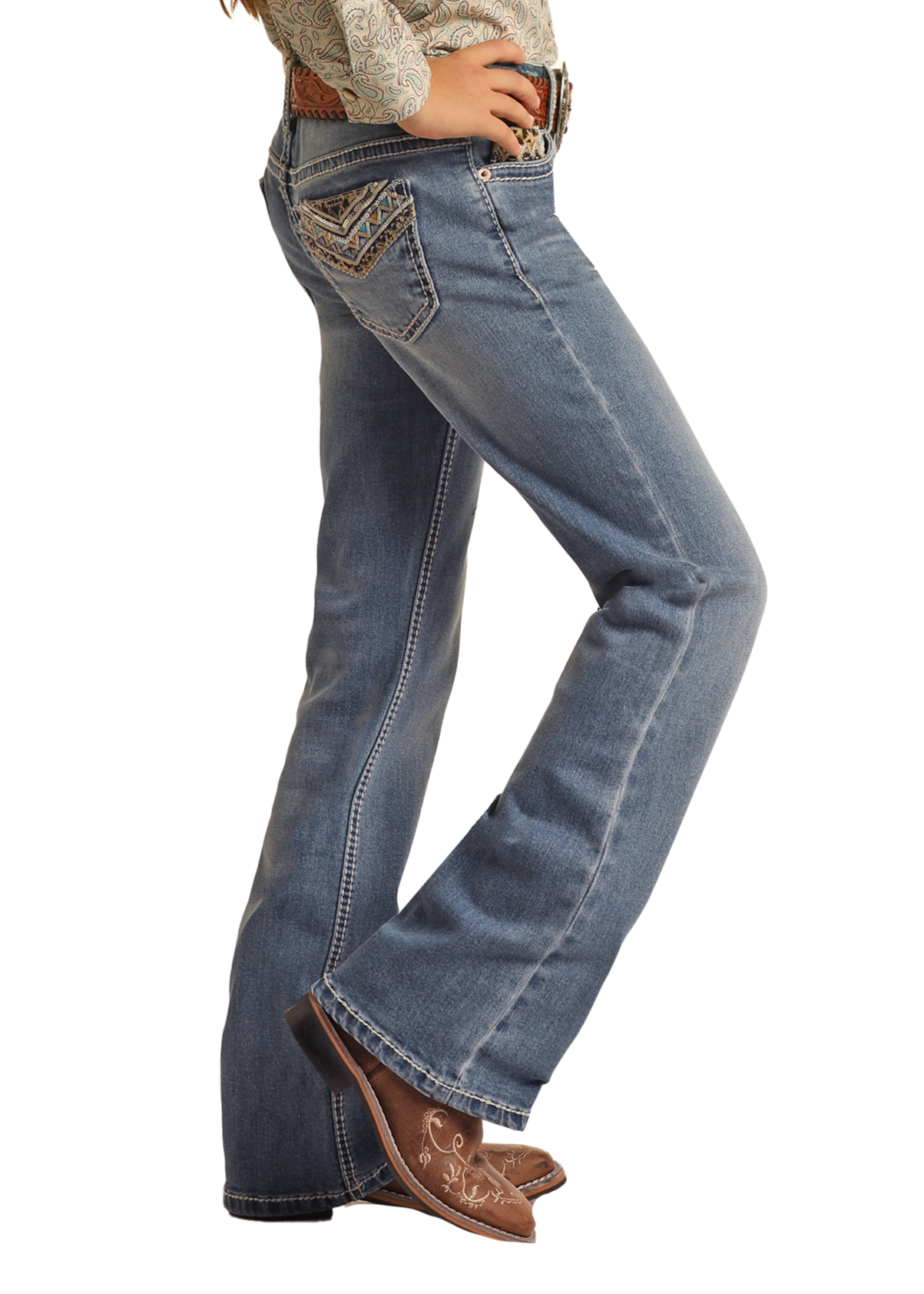 A girl wearing Rock & Roll Denim Girls' Leopard Embroidered Pocket Bootcut Jeans and brown cowboy boots stands sideways with her hands on her hips.