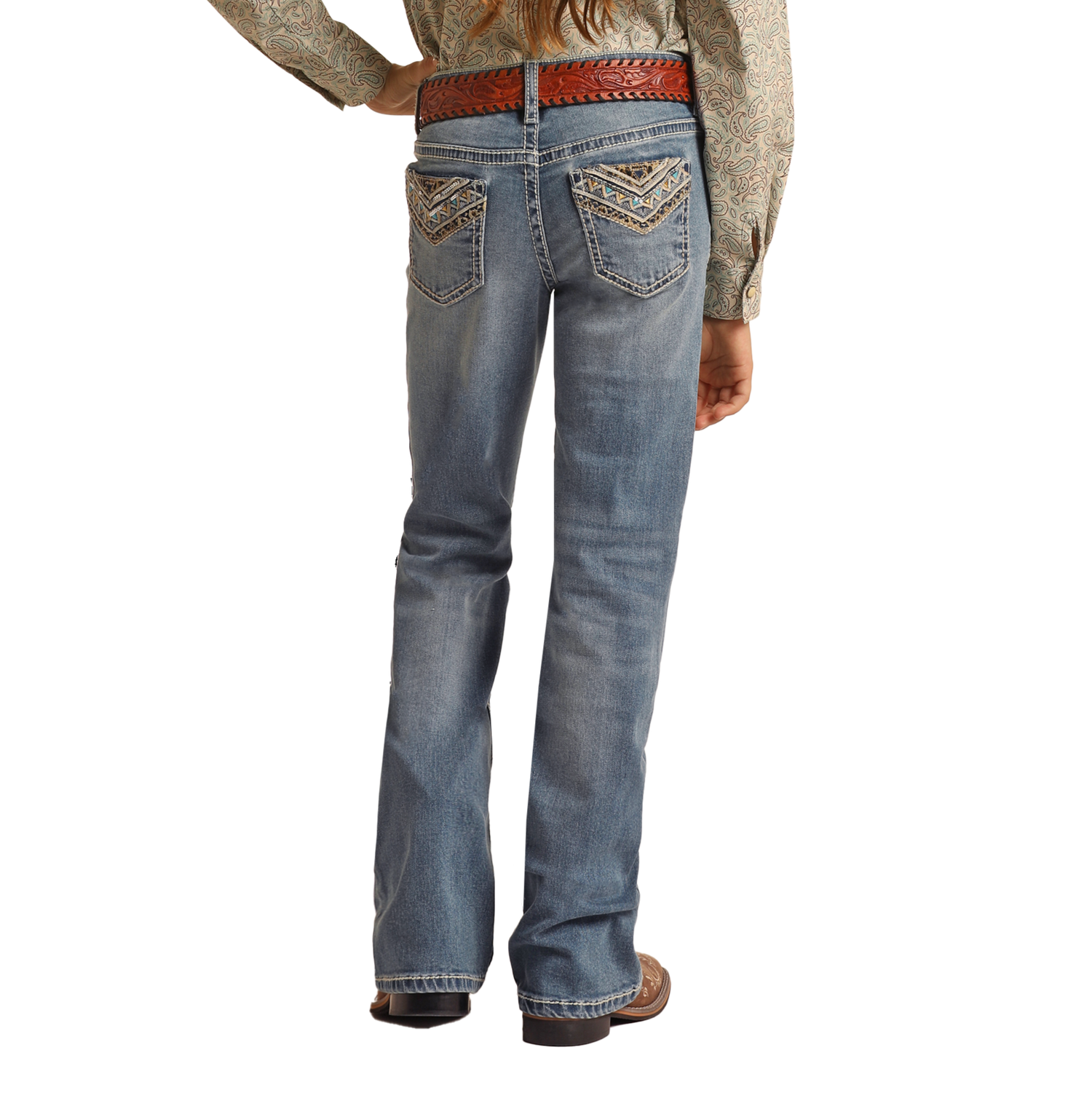 A person wearing a paisley shirt, Rock & Roll Denim Girls' Leopard Embroidered Pocket Bootcut Jeans, a brown woven belt, and brown shoes is shown from the back with one hand on their hip.