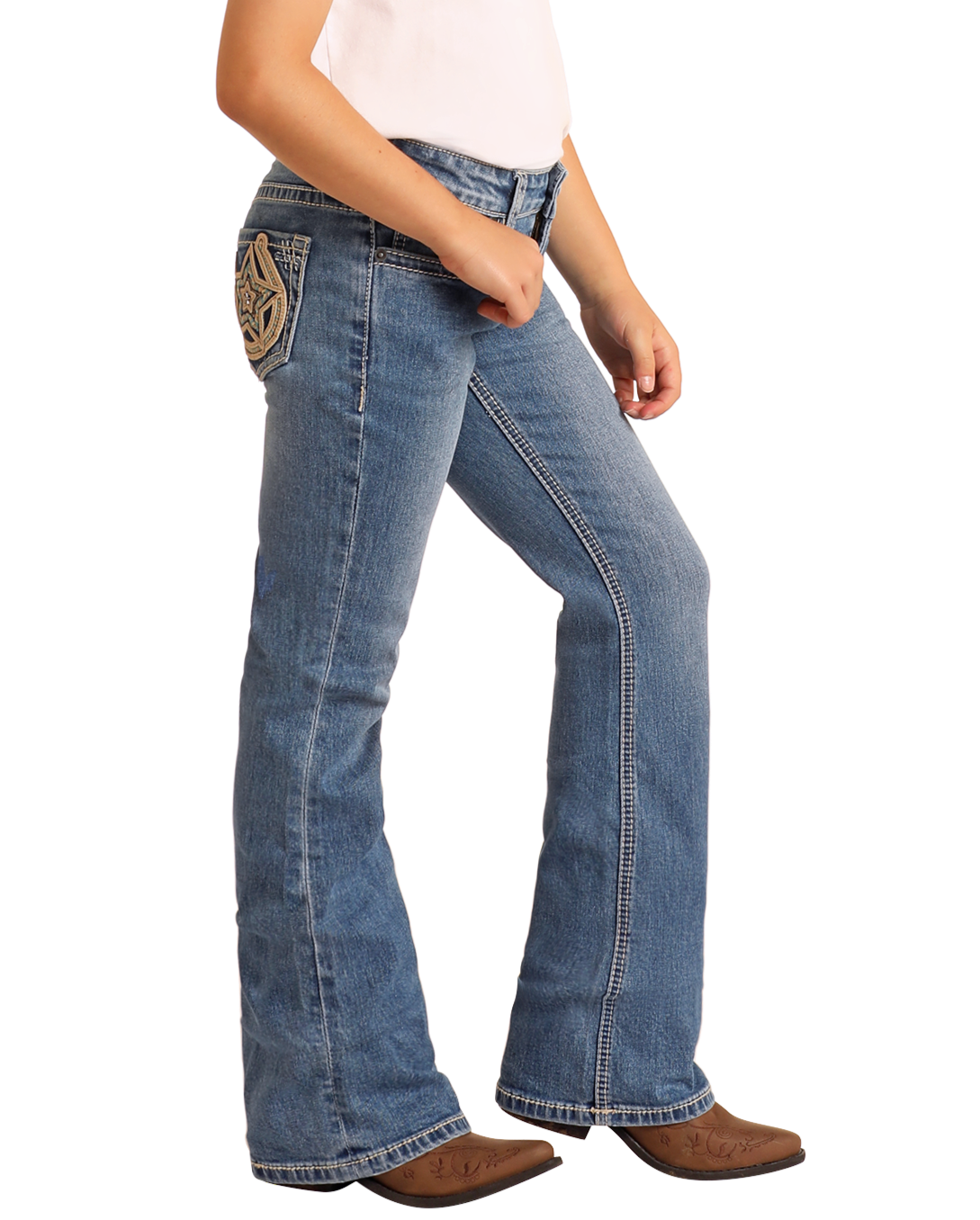 A girl wears Rock & Roll Denim Girls' Mid Rise Extra Stretch Horseshoe Star Bootcut Jeans with decorative stitching, a light top, and brown cowboy boots, standing against a plain white background.