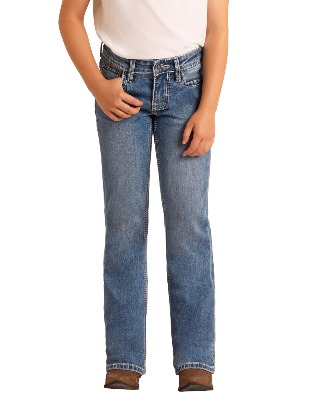 A girl models Rock & Roll Denim Girls' Mid Rise Extra Stretch Horseshoe Star Bootcut Jeans, paired with a white shirt and brown shoes, standing against a light background. Only her lower torso and legs are shown.