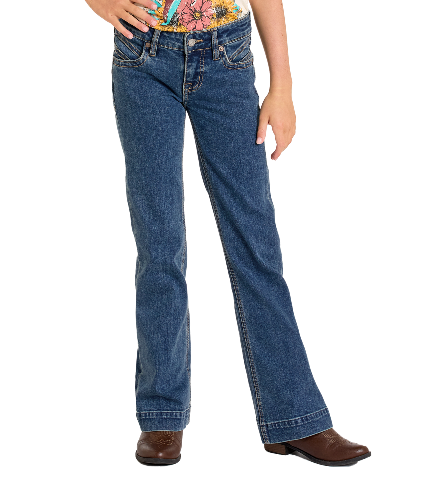 A person stands with one hand on their hip wearing Rock & Roll Denim Girls' Signature Stitch Trouser Jeans, a colorful floral shirt, and brown boots. The image captures them from shoulders to feet.