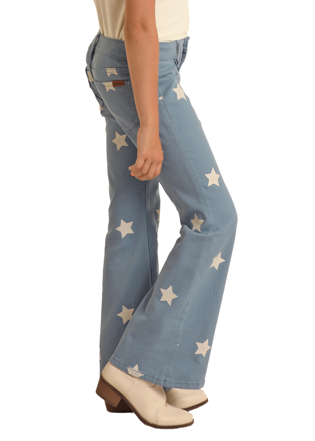 A person wearing Rock & Roll Denim Girls' Star Print Flare Jeans with white stars and cream heeled boots stands sideways against a plain background.