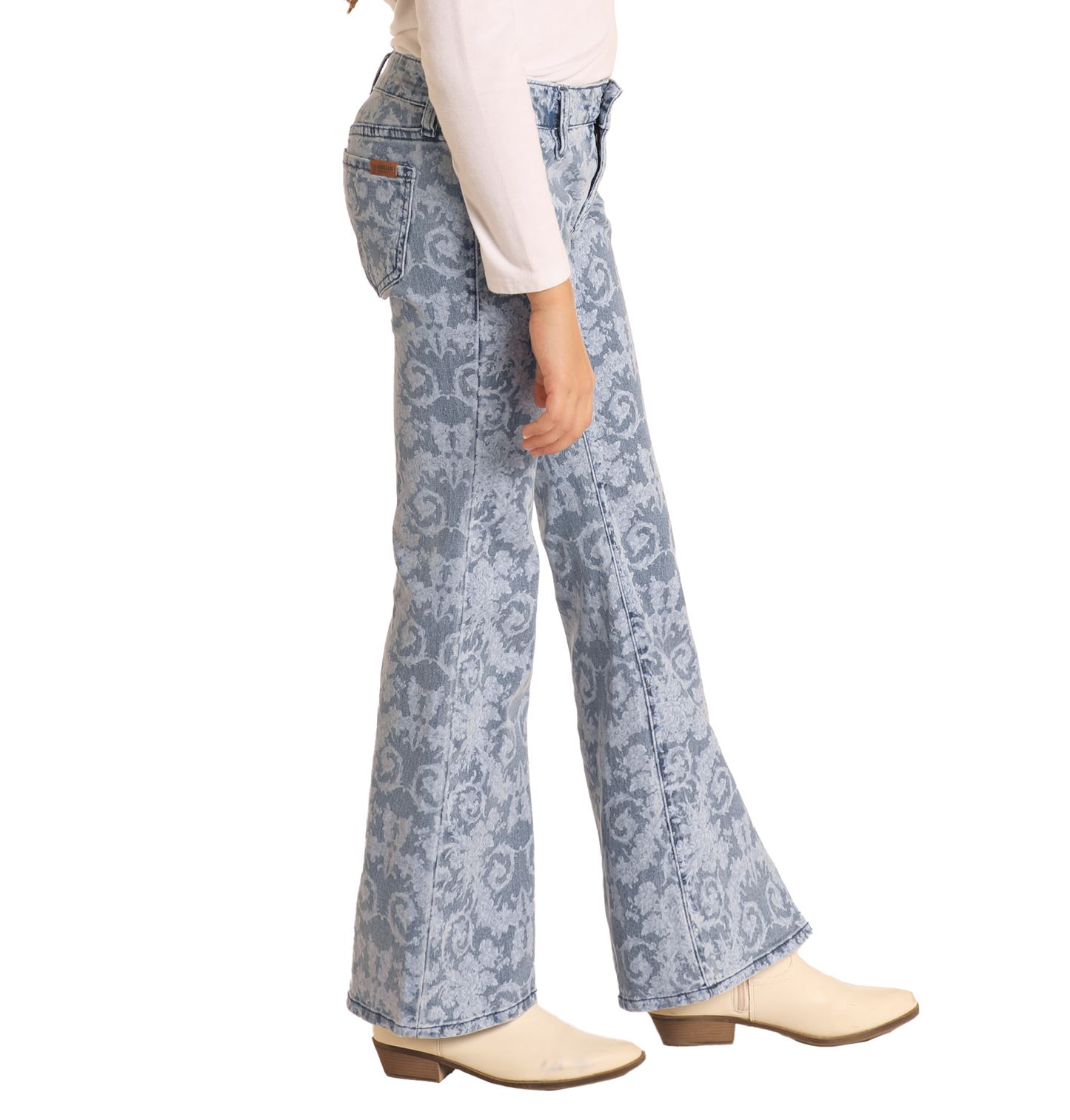 A person models the Rock & Roll Denim Girls' Floral Print Flare Jeans with a white long-sleeve shirt and cream heeled boots, standing sideways against a white background.