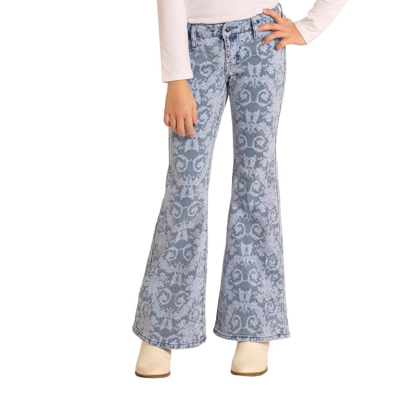 A girl models the Rock & Roll Denim Girls' Floral Print Flare Jeans with a long-sleeve white top and cream shoes, posing with one hand on her hip against a plain white background.