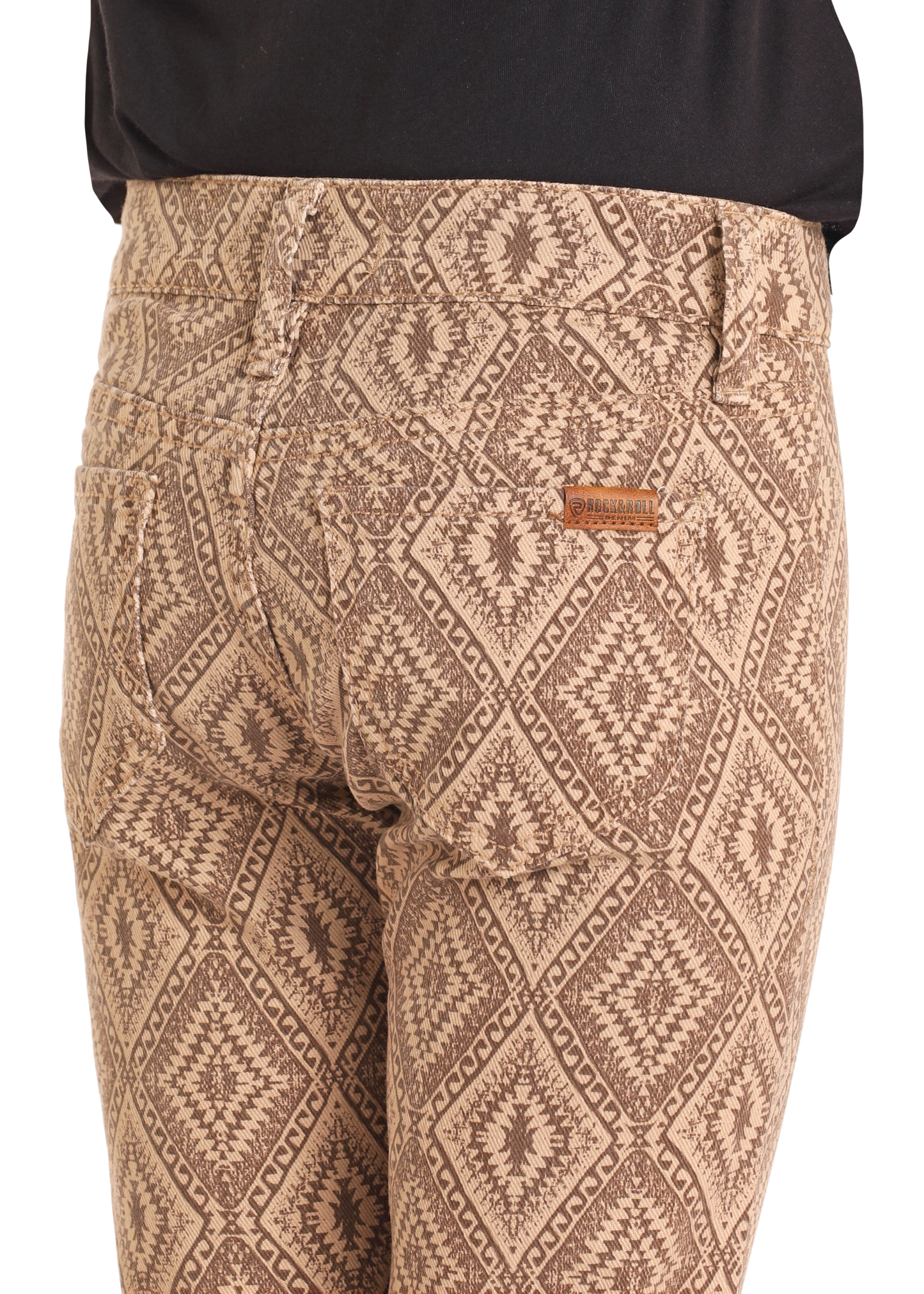 Close-up of a person wearing Rock & Roll Denim Girls' Tan Aztec Button Flare Jeans with a geometric diamond pattern and brown brand tag near the pocket, styled with a black top for a trendy cowgirl look.