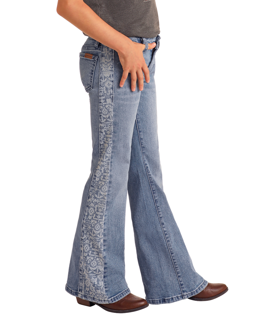 A girl models Rock & Roll Denim's Girls' Aztec Panel Button Flare Jeans, featuring a decorative patterned stripe, brown boots, and a dark shirt, showcasing Southwestern style against a plain white background.