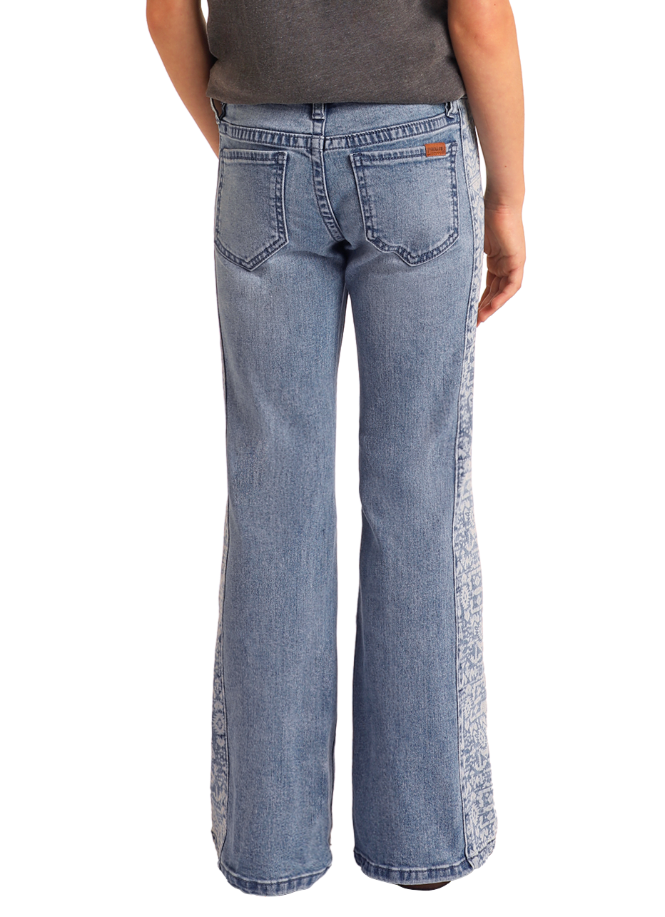 A person is seen from behind wearing Rock & Roll Denim Girls' Aztec Panel Button Flare Jeans, featuring light blue denim, Southwestern-inspired side panels, two back pockets, and a brown waistband patch.