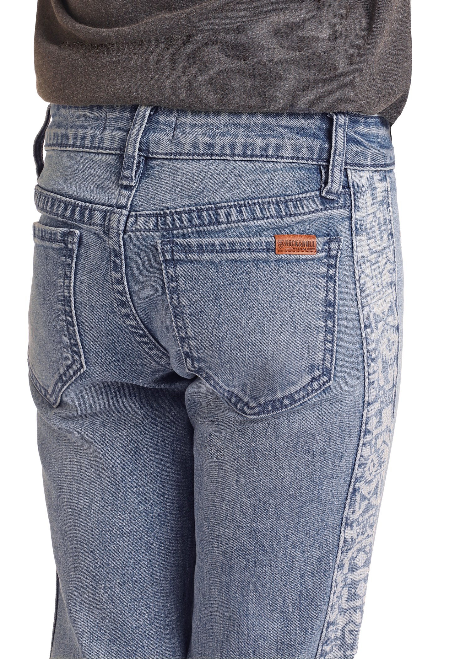 Close-up of a person wearing Rock & Roll Denim Girls' Aztec Panel Button Flare Jeans in light blue, featuring a faded patterned side panel and a small brown label above the right pocket. A tucked-in dark shirt completes the Southwestern look.