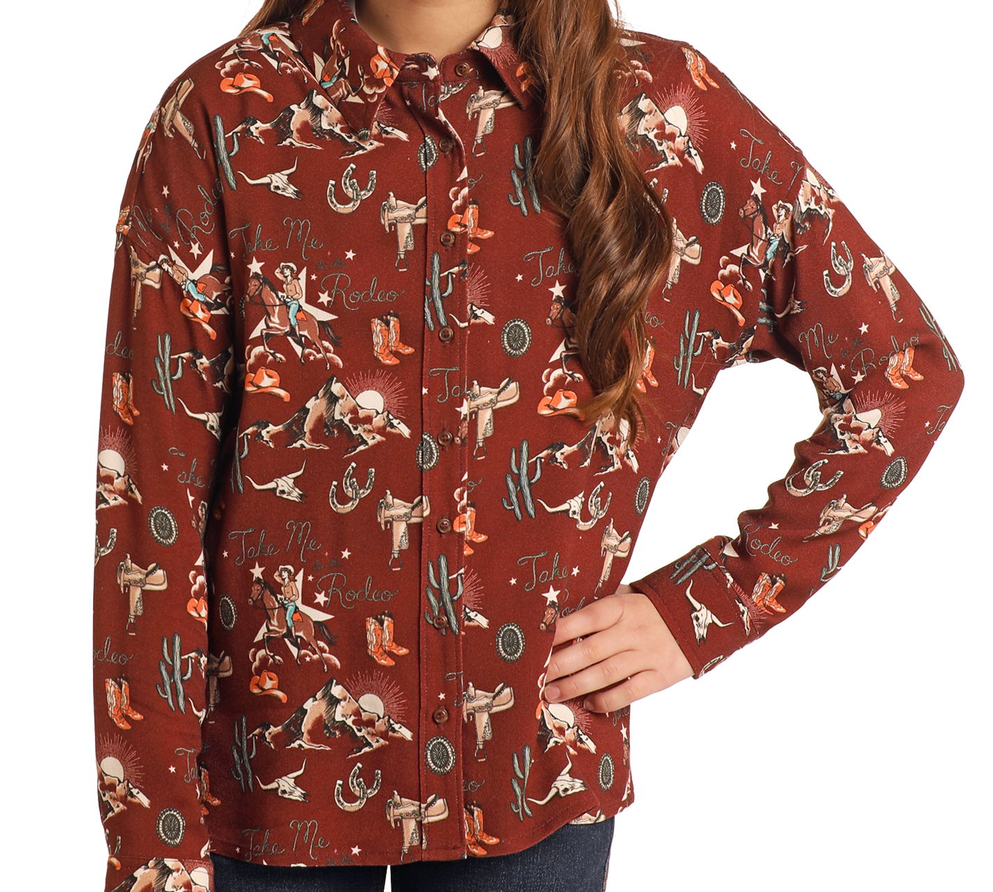 A girl sports the Rock & Roll Denim Girls' Retro Conversational Overshirt, featuring a rodeo-themed print with cowboys, boots, cacti, and “Take Me to the Rodeo”—a standout Western shirt with her hand on her hip.