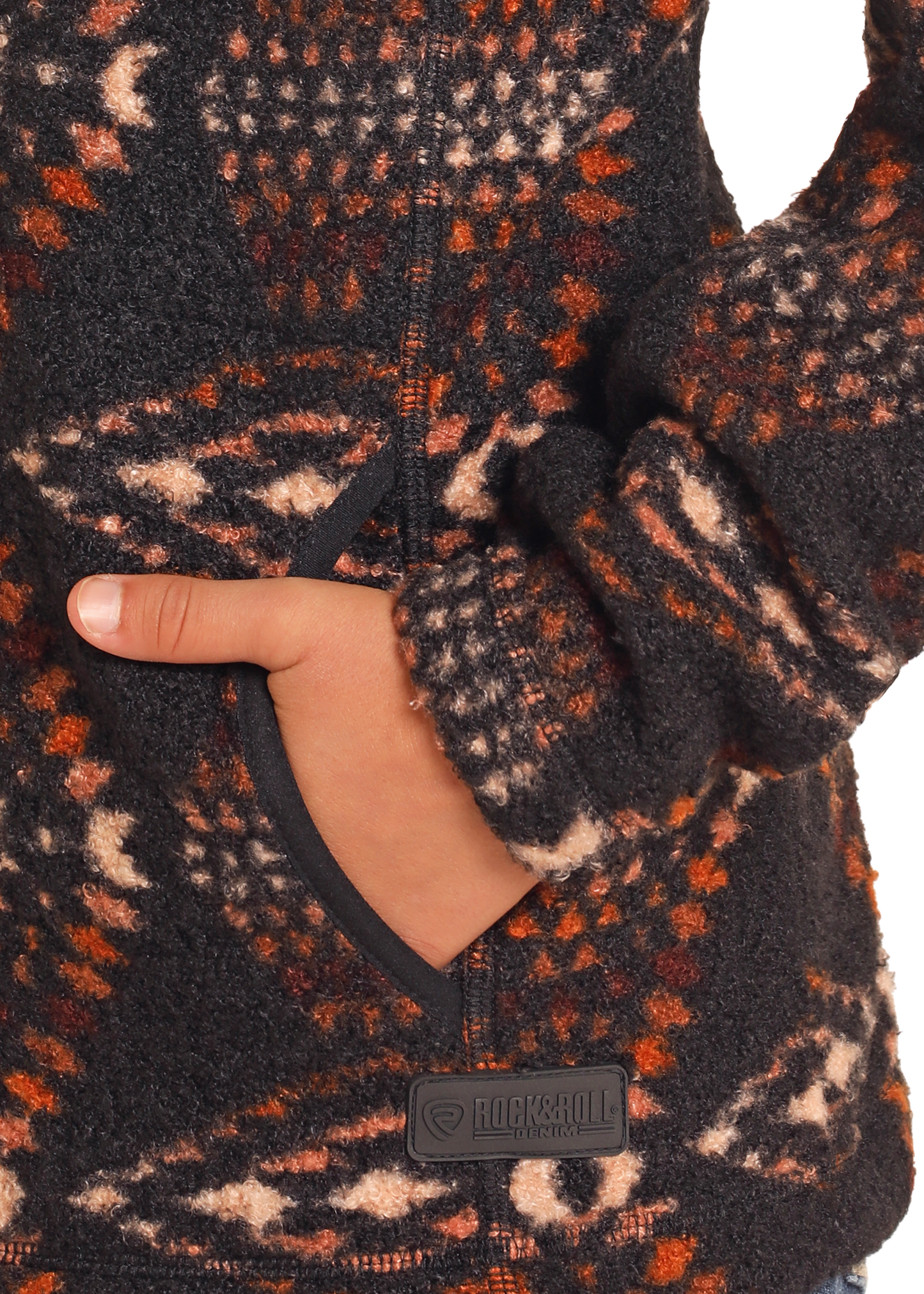 A close-up shows a hand in the pocket of the fuzzy Kids' Aztec Print Quarter Zip Pullover by Rock & Roll Denim, detailed with black, orange, and beige geometric patterns. The "Rock & Roll Denim" patch appears near the pocket.