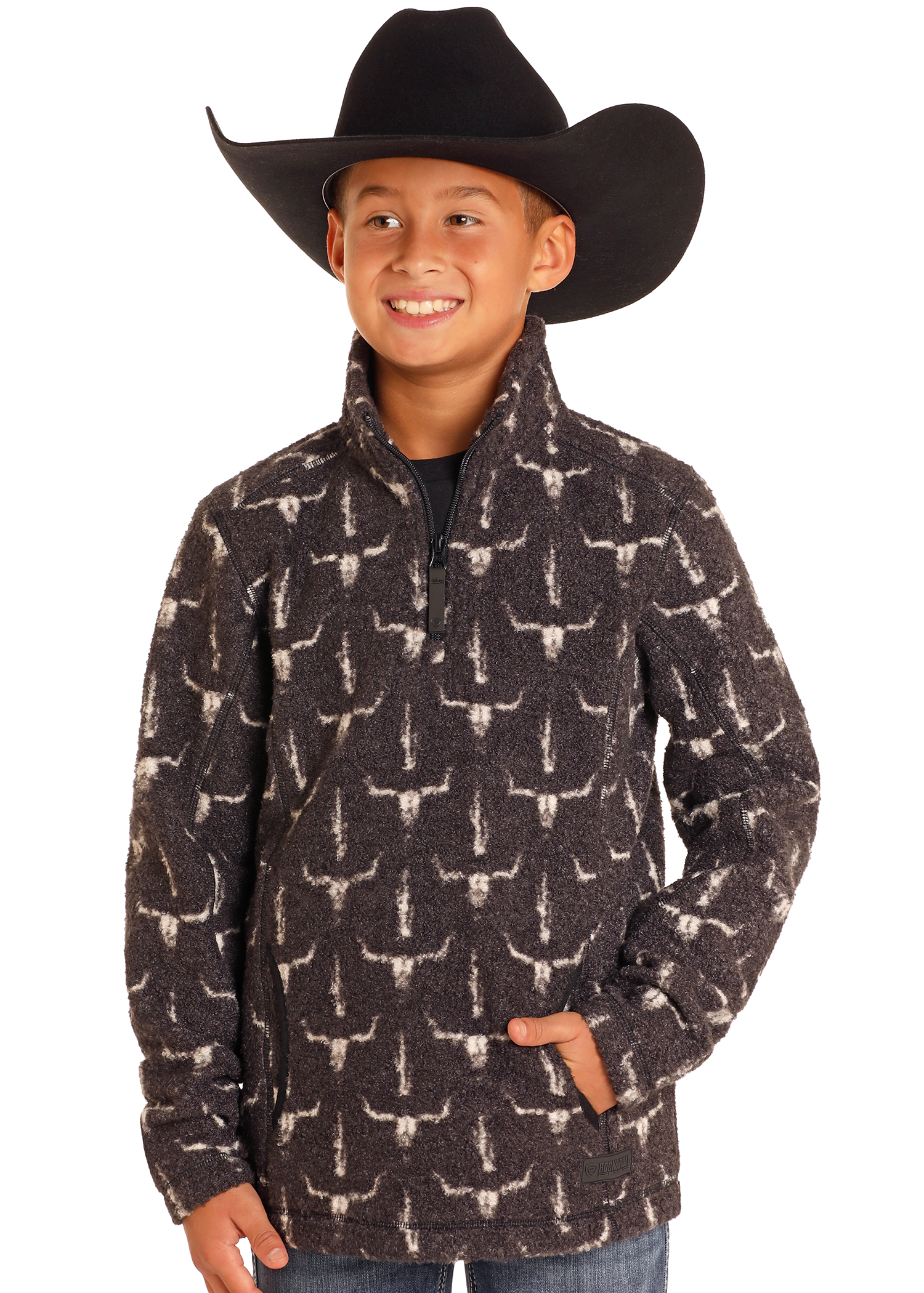 A smiling child in a large black cowboy hat and the Rock & Roll Denim Kids' Steer Skull Quarter Zip Pullover, hands in pockets, stands against a plain white background.