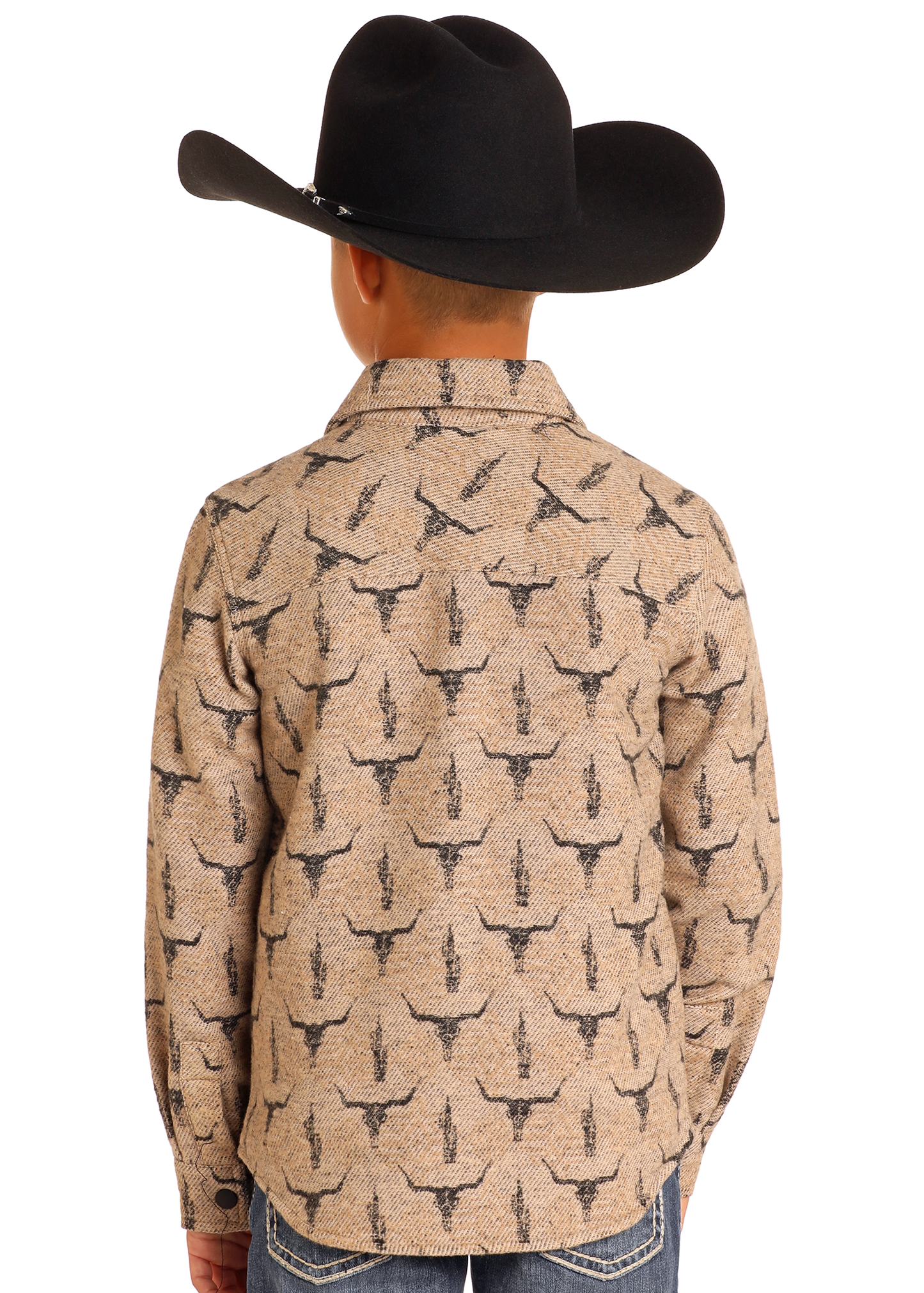 A child models the Rock & Roll Denim Kids' Steer Skull Shirt Jacket, featuring a tan color with a black steer skull print and a black cowboy hat, shown from behind with hands in pockets against a plain white background.