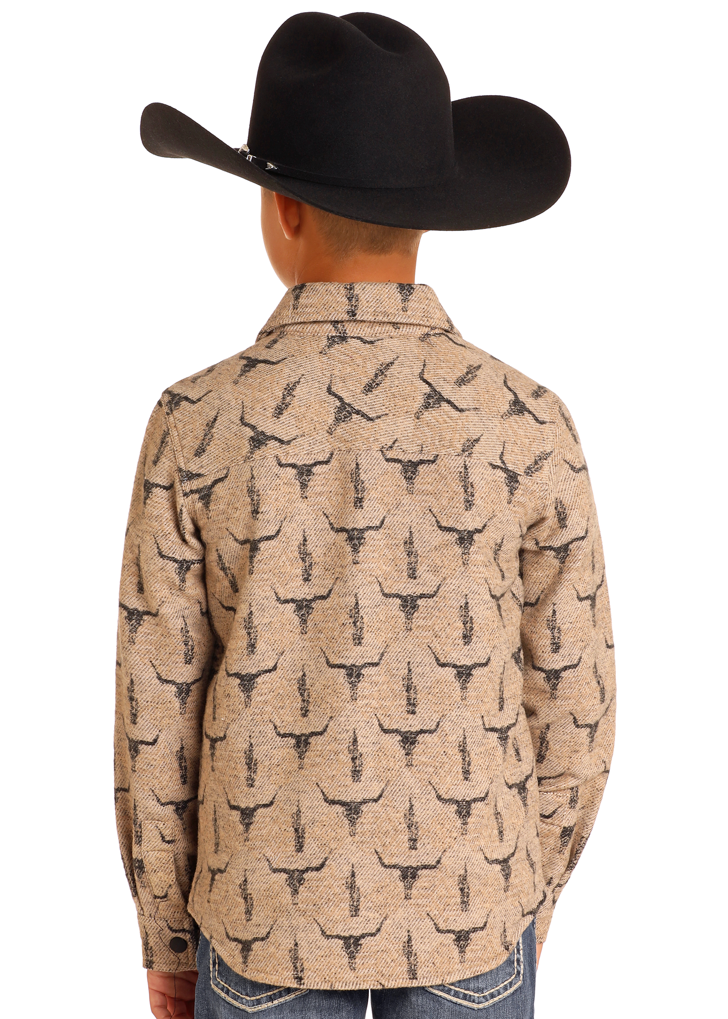 A child models the Rock & Roll Denim Kids' Steer Skull Shirt Jacket, featuring a tan color with a black steer skull print and a black cowboy hat, shown from behind with hands in pockets against a plain white background.