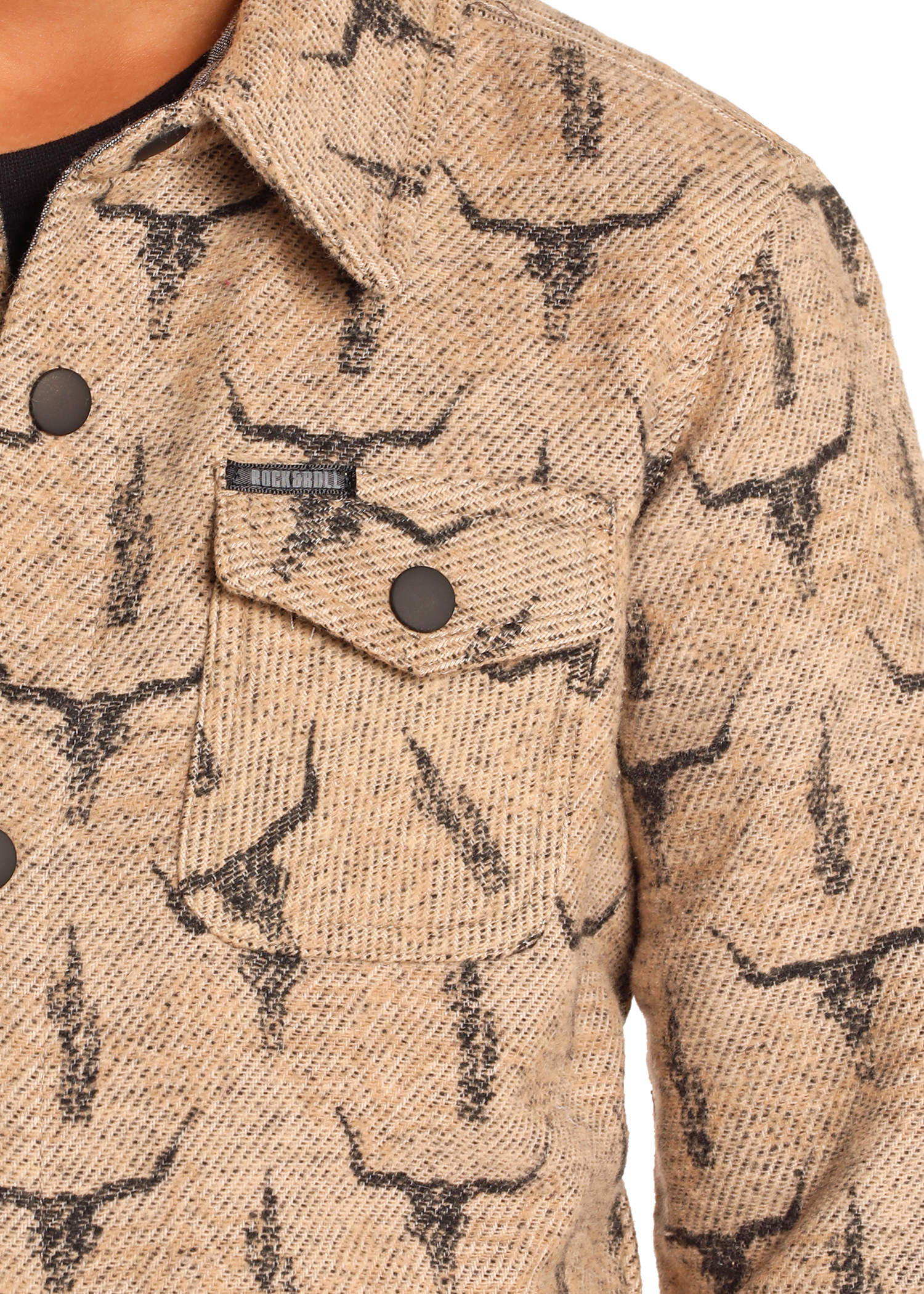 Close-up of the Rock & Roll Denim Kids' Steer Skull Shirt Jacket, showcasing a steer skull print, front flap pocket with two buttons, and a small rectangular label above the pocket on textured tan fabric.