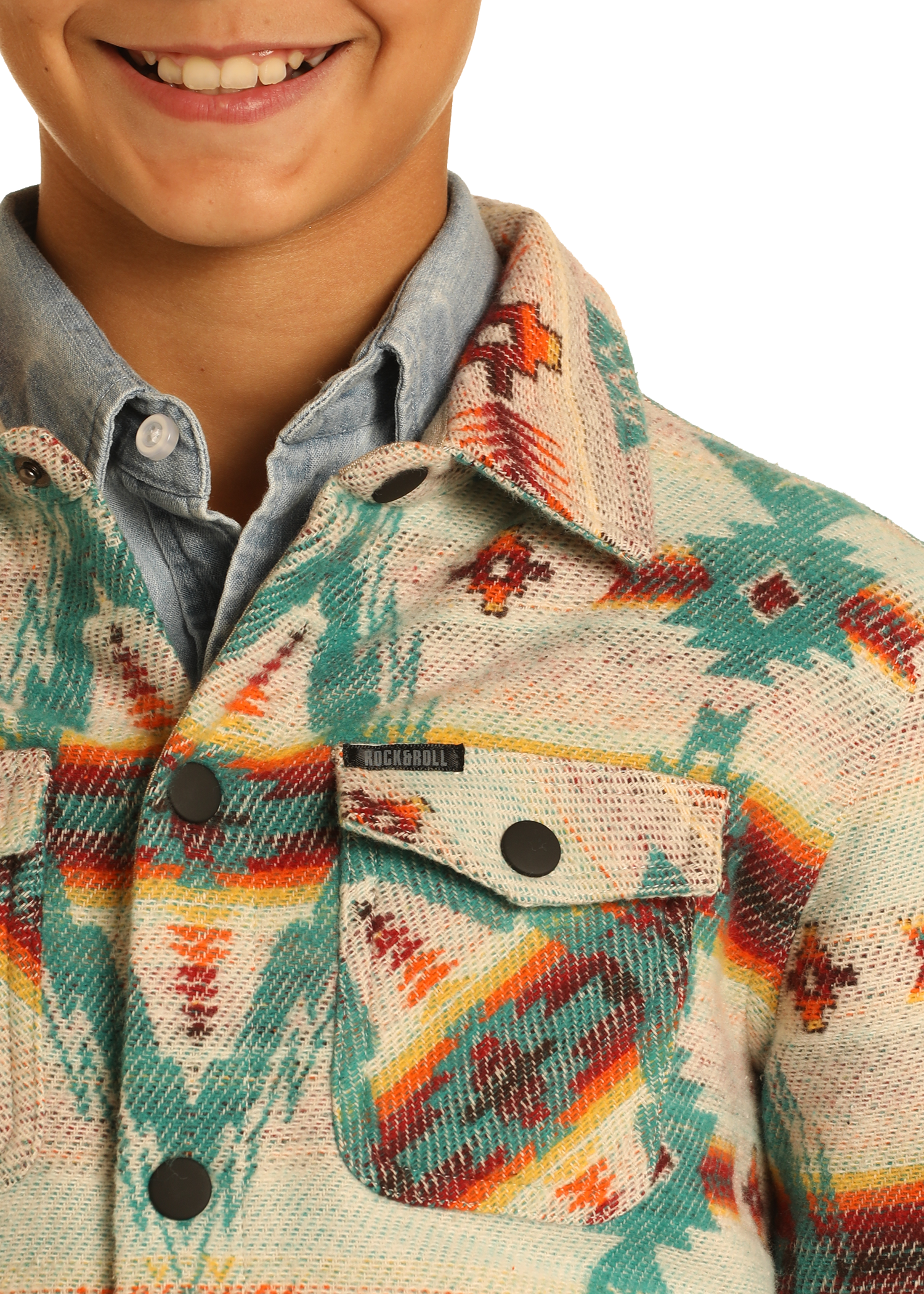 A close-up of a smiling child in the Rock & Roll Denim Kids' Cream Aztec Jacquard Shirt Jacket, featuring turquoise, orange, and red designs over a blue button-up, with focus on the 100% cotton jacket’s front pocket and collar.