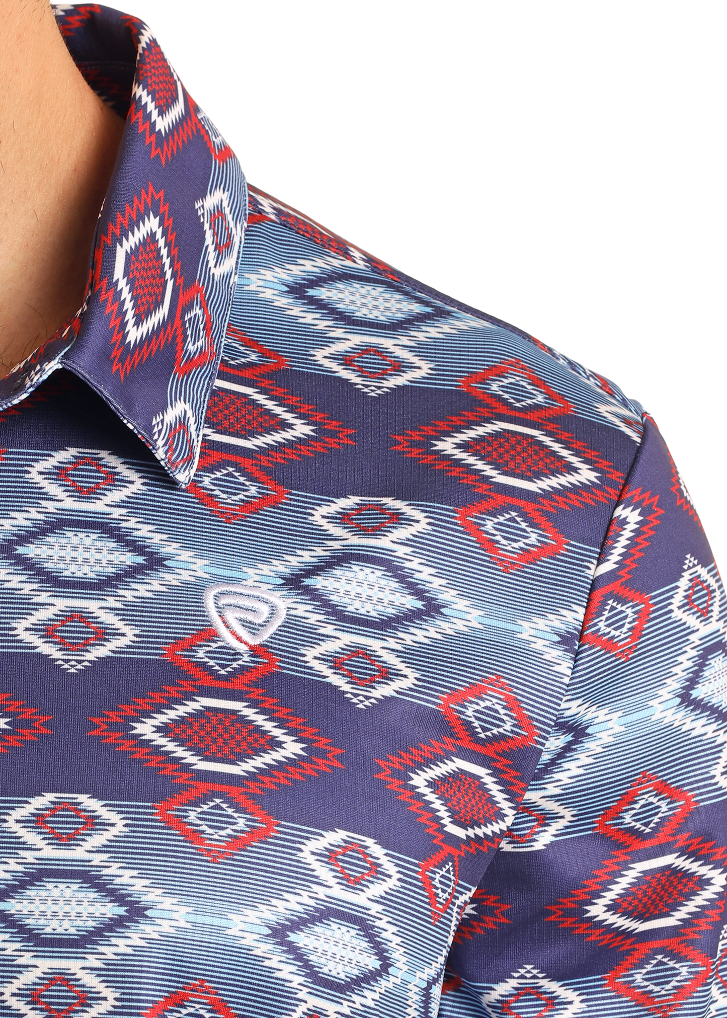 Close-up of the Rock & Roll Denim Navy Aztec Print Polo, featuring a colorful red, white, and blue geometric diamond pattern. This regular fit polo has a collar and offers a casual look with part of the wearer’s neck and shoulder visible.