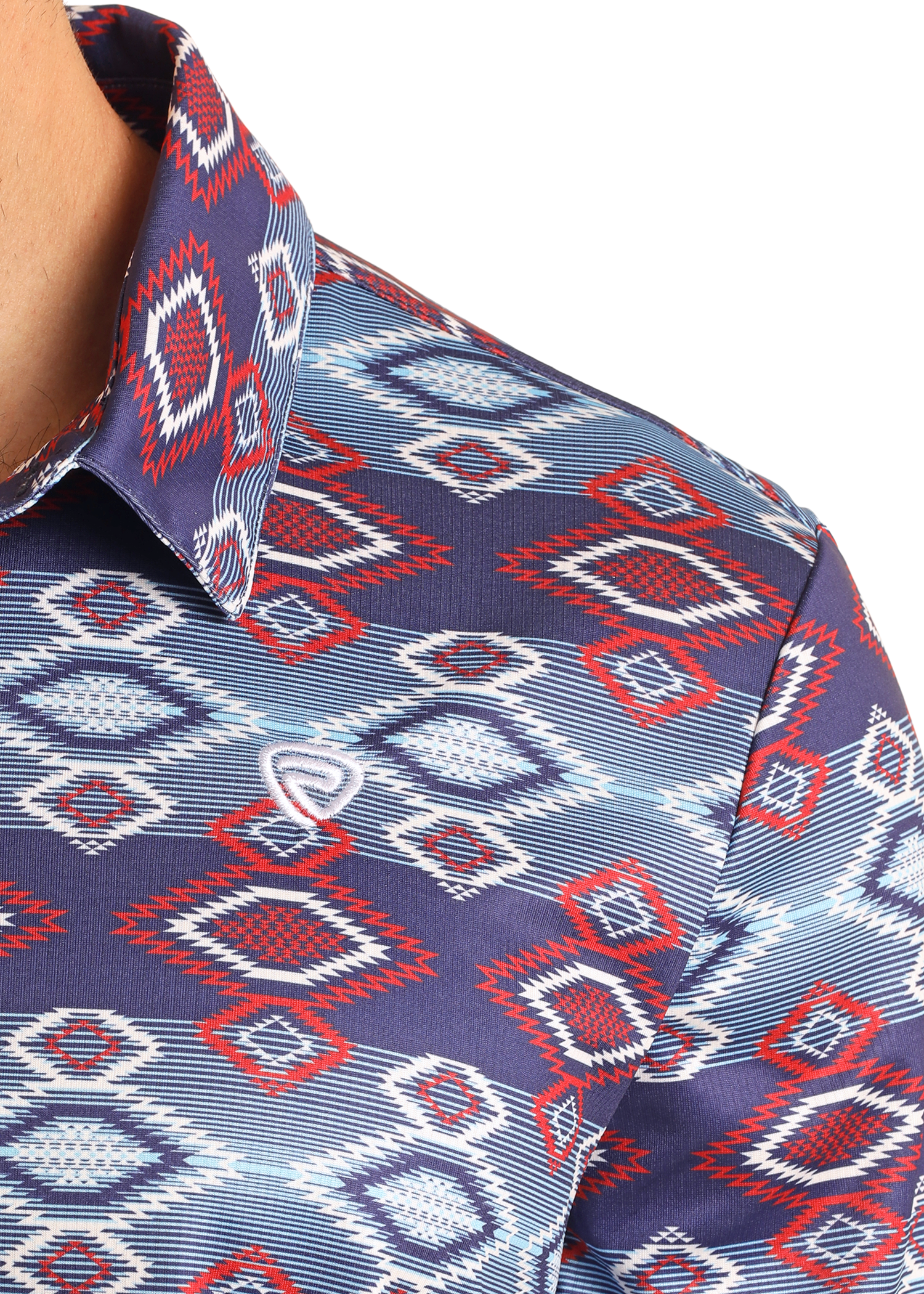 Close-up of the Rock & Roll Denim Navy Aztec Print Polo, featuring a colorful red, white, and blue geometric diamond pattern. This regular fit polo has a collar and offers a casual look with part of the wearer’s neck and shoulder visible.